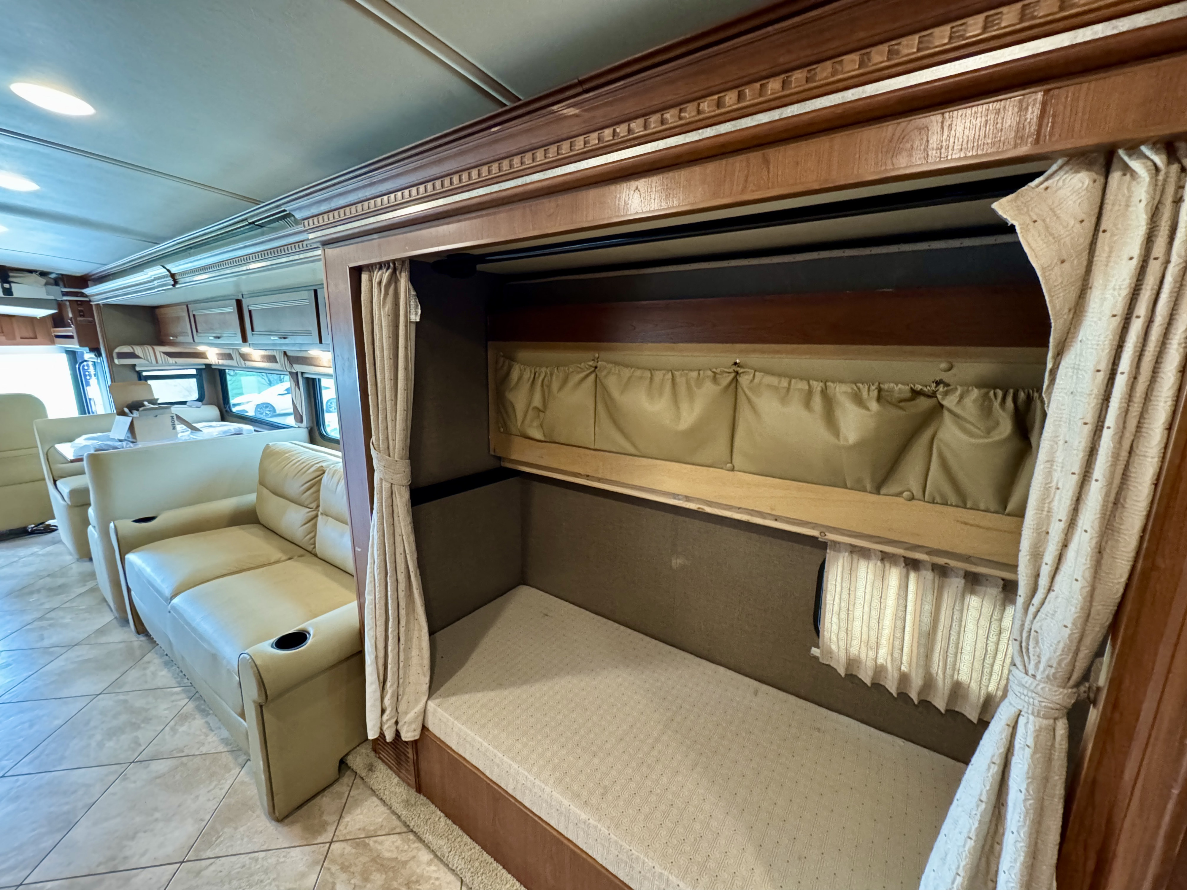 Spacious RV rental interior featuring a cozy bunk bed with privacy curtains, light-colored sofas, and a dining area.. Winnebago Forza 2017