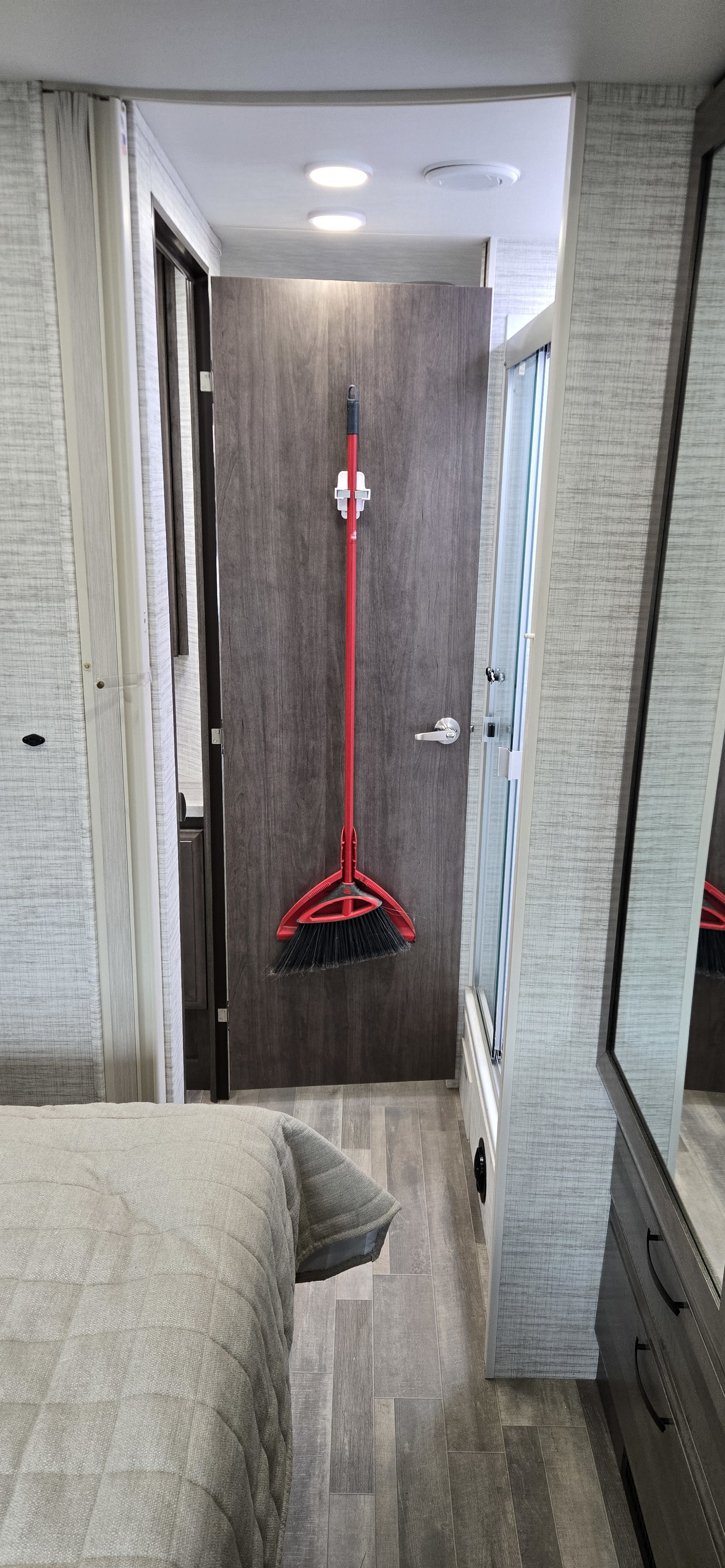 Compact RV rental interior: red broom on door, bed, shower, and mirrored dresser. Practical and space-saving.. Jayco Greyhawk 2025