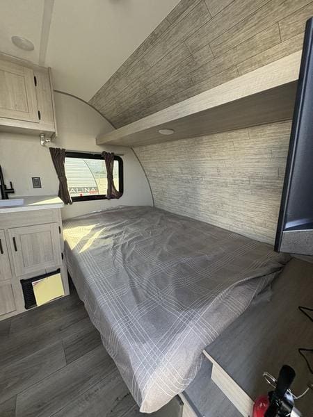Cozy RV rental bedroom with gray plaid bed, wood-paneled walls/ceiling, a window, and storage cabinets. Perfect for travel.. 5ZT2CABC9TK012992 Catalina 2026