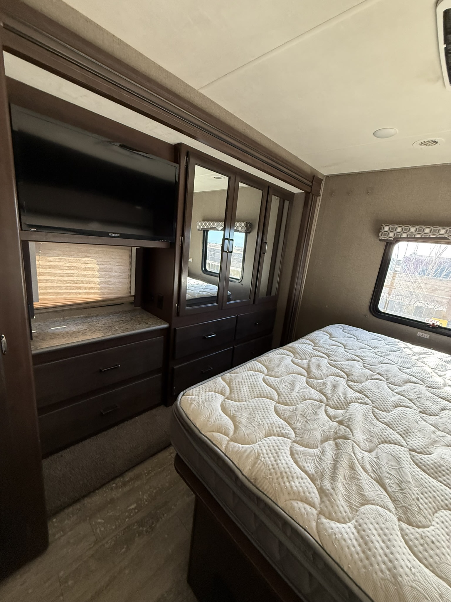 Spacious RV rental bedroom featuring a queen mattress, dark wood storage, mounted TV, and a window for natural light.. Thor Hurricane 2020