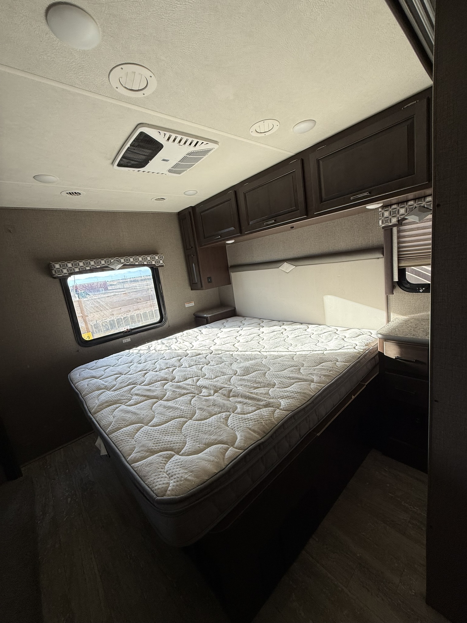 This RV rental bedroom features a plush mattress, overhead cabinets, a window with a view, and ceiling AC/lighting.. Thor Hurricane 2020