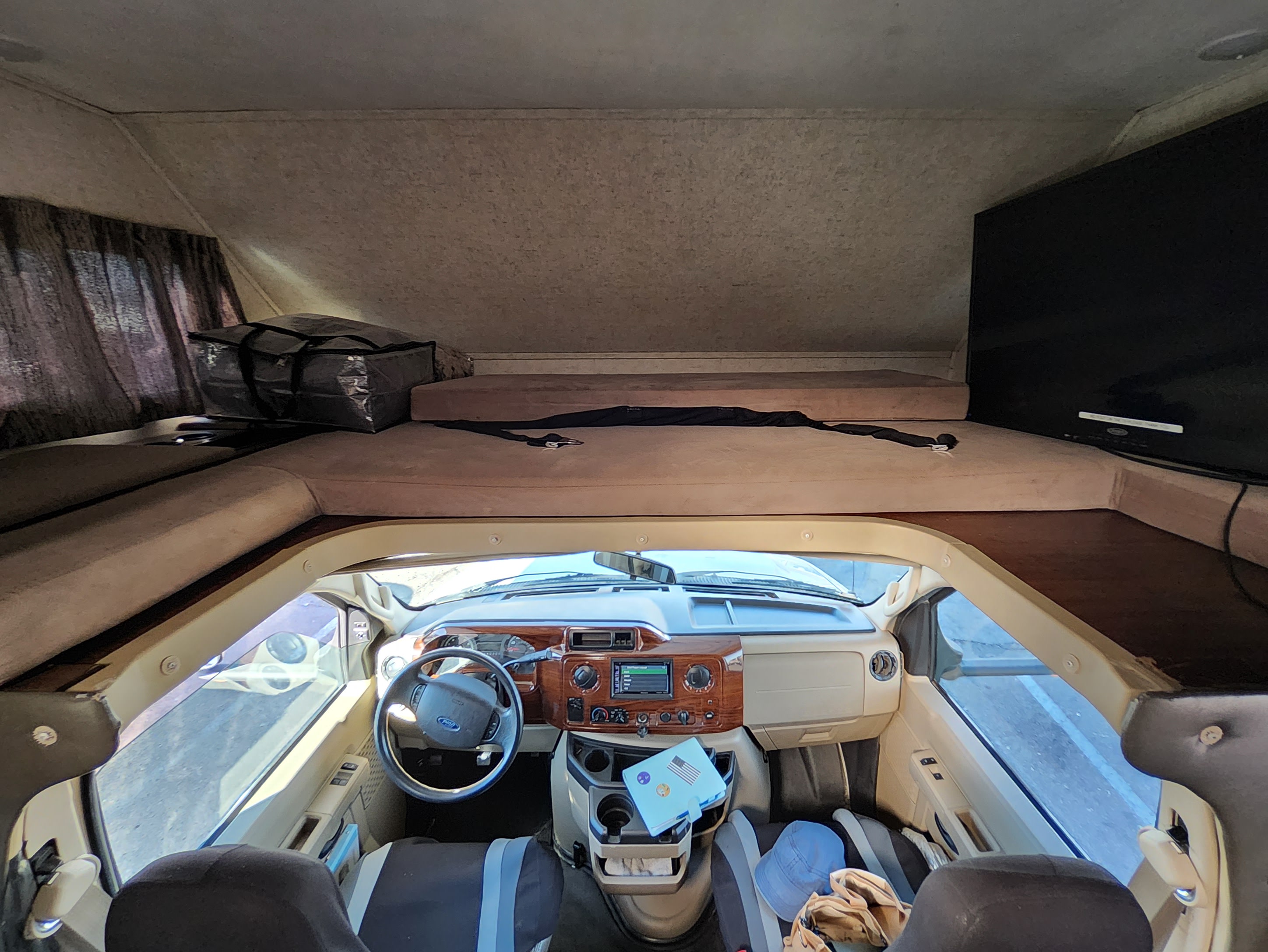 RV rental interior: driver's cab with steering wheel, dashboard, and an overhead bunk with mattress, TV. Ready for road trip travel.. Forest River Other 2018