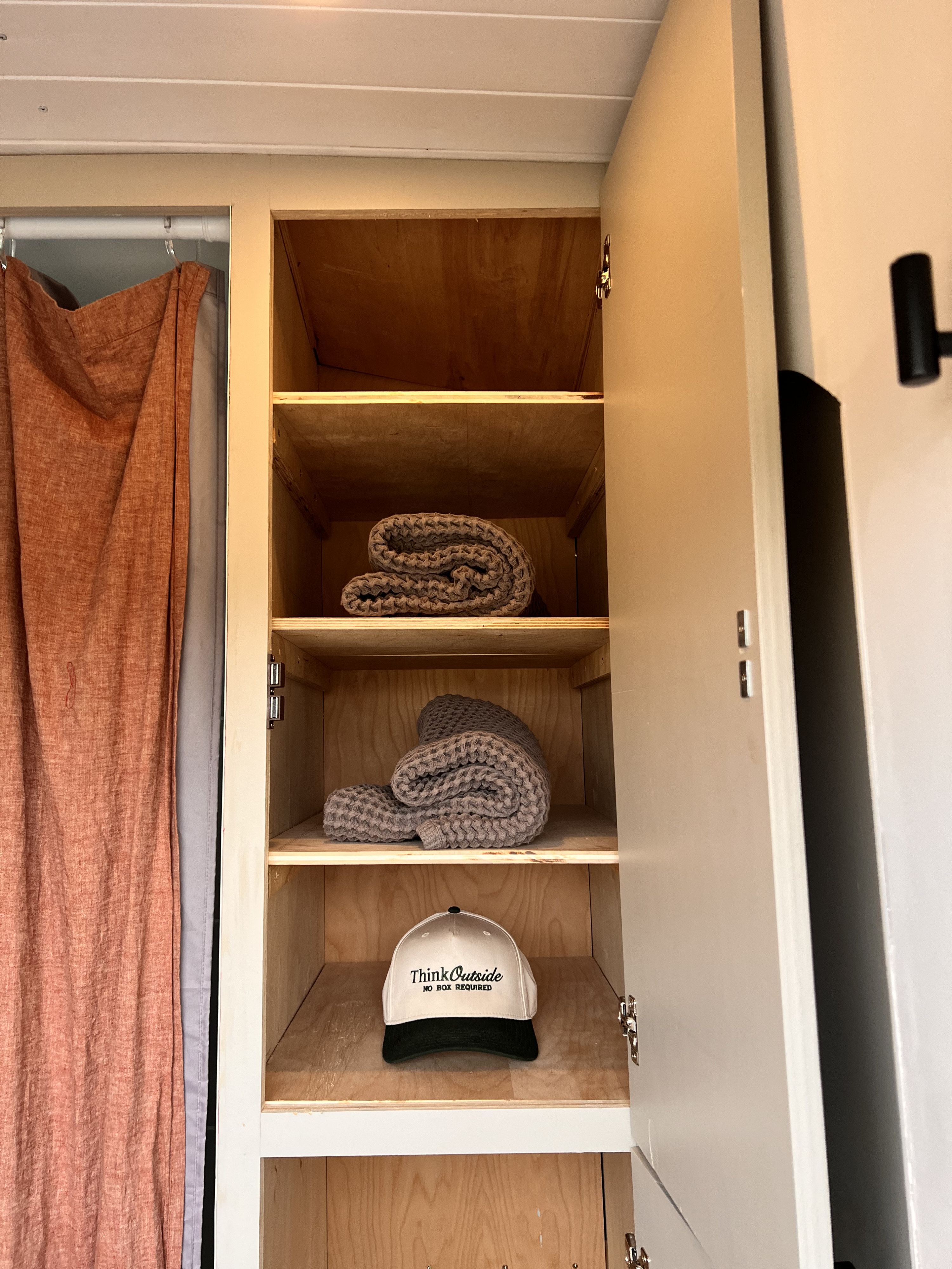 RV rental storage: Open cabinet with shelves, folded blankets, and a "Think Outside" cap. Ideal for travel prep.. Ford Transit XL 2017