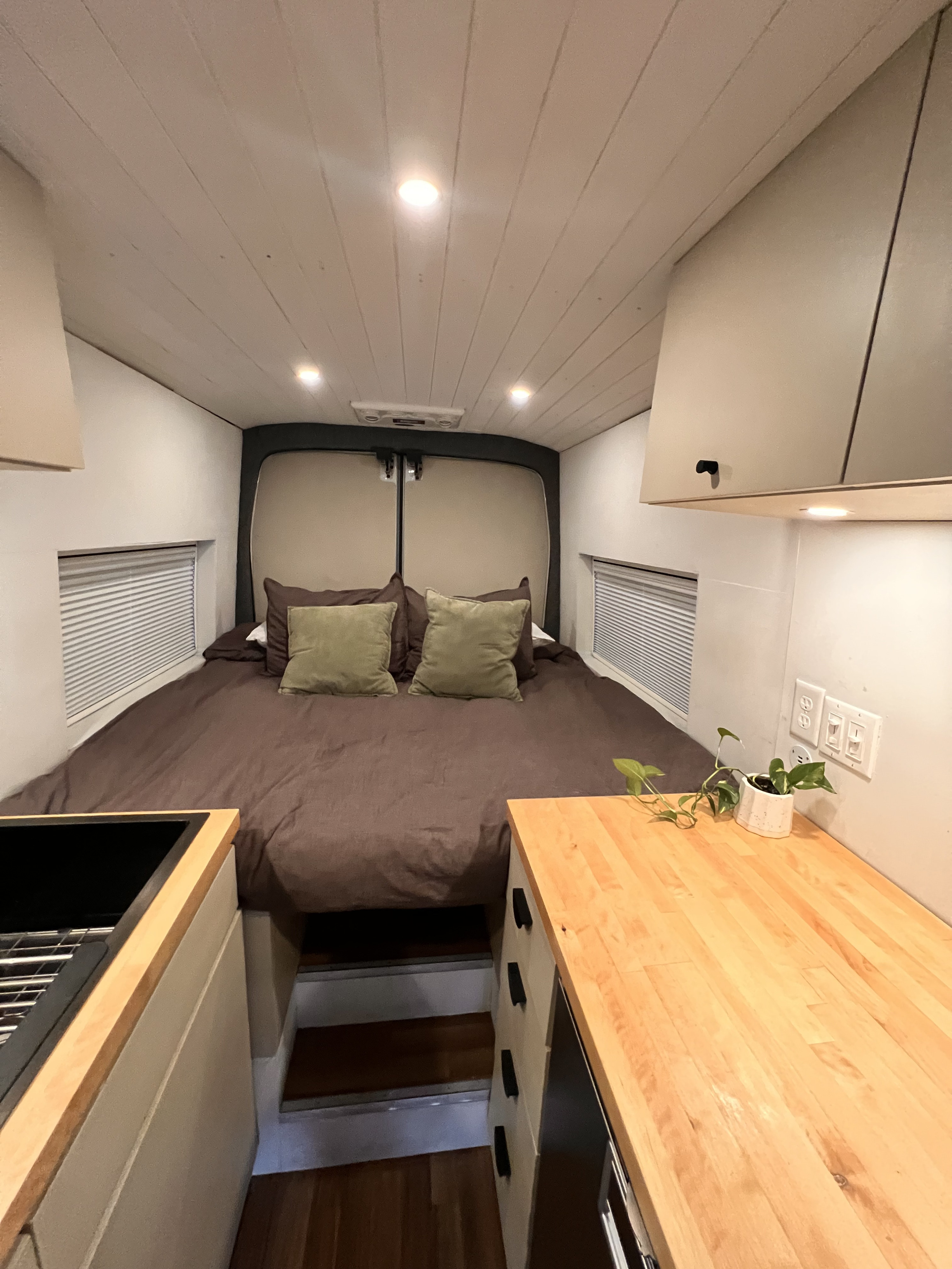 Inside a modern rv rental: full bed, wood counters, and recessed lighting in a compact camper van conversion.. Ford Transit XL 2017