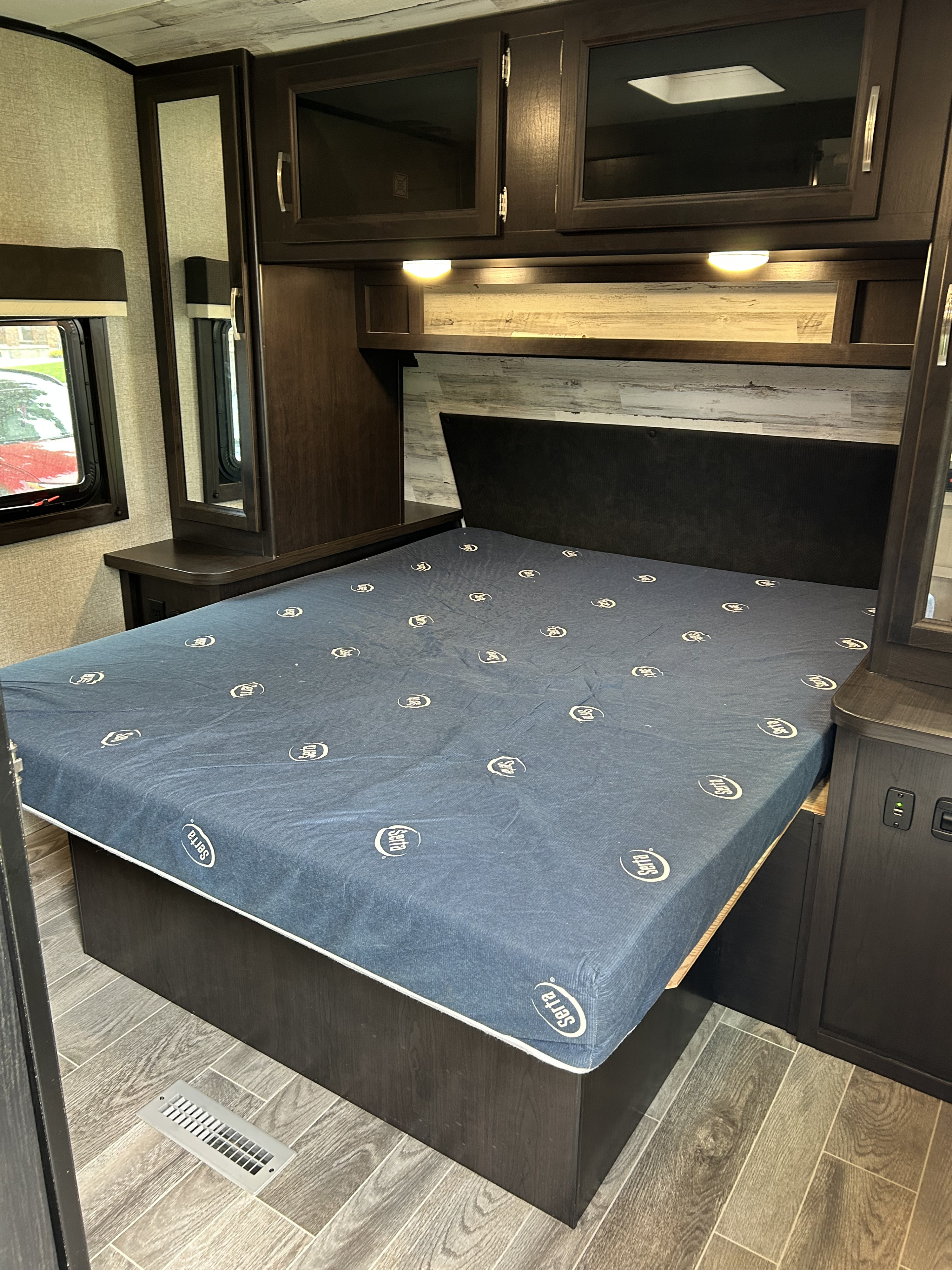 Interior of a modern RV rental bedroom, featuring a Serta mattress, dark wood cabinetry, and essential bedside features.. Jayco Jay Feather 2020