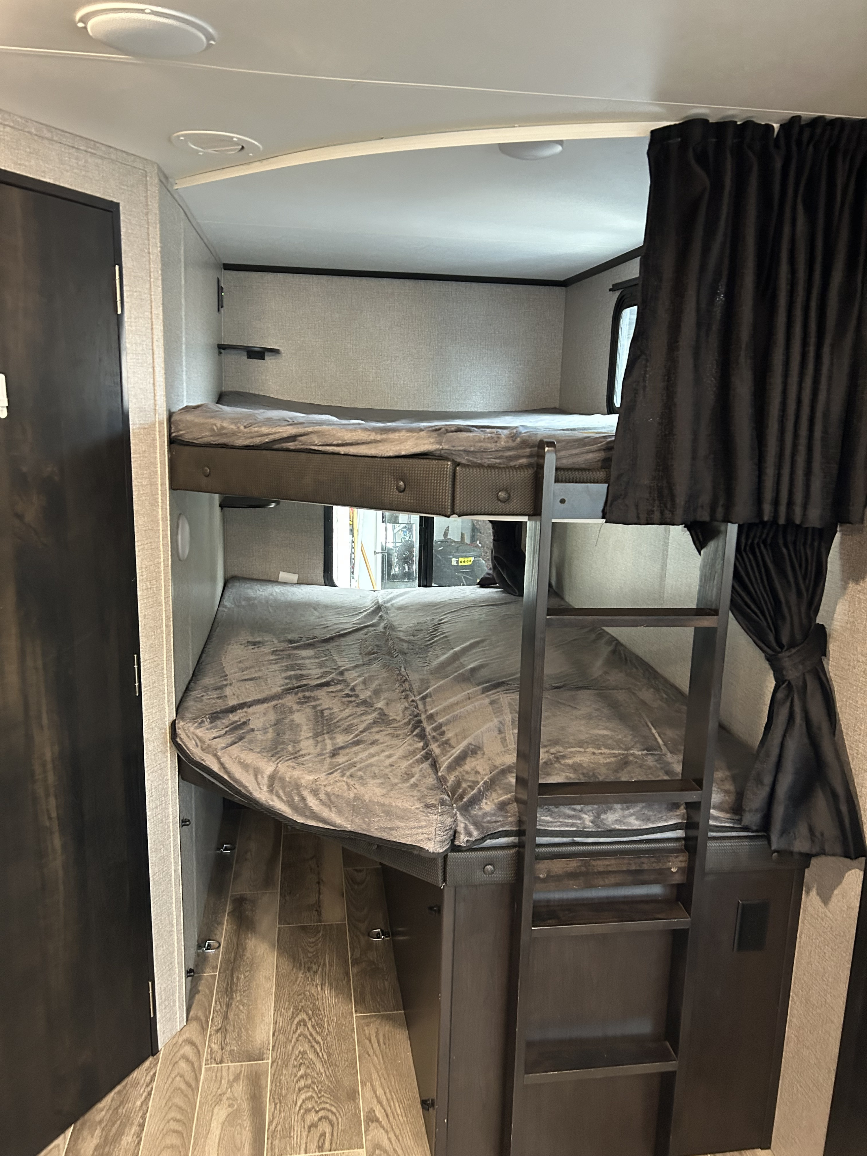 Modern RV rental bunk beds, equipped with a ladder and dark privacy curtains, provide a compact sleeping area.. Jayco Jay Feather 2020