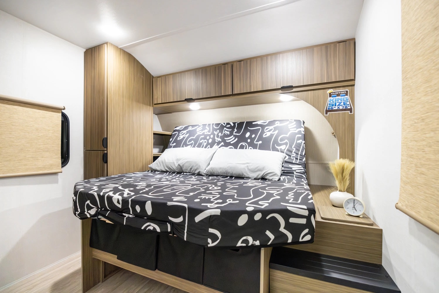 RV rental bedroom: A compact space with a king-size bed (black/white pattern), sleek wood cabinets, and ambient lighting.. Forest River Wildwood 2025