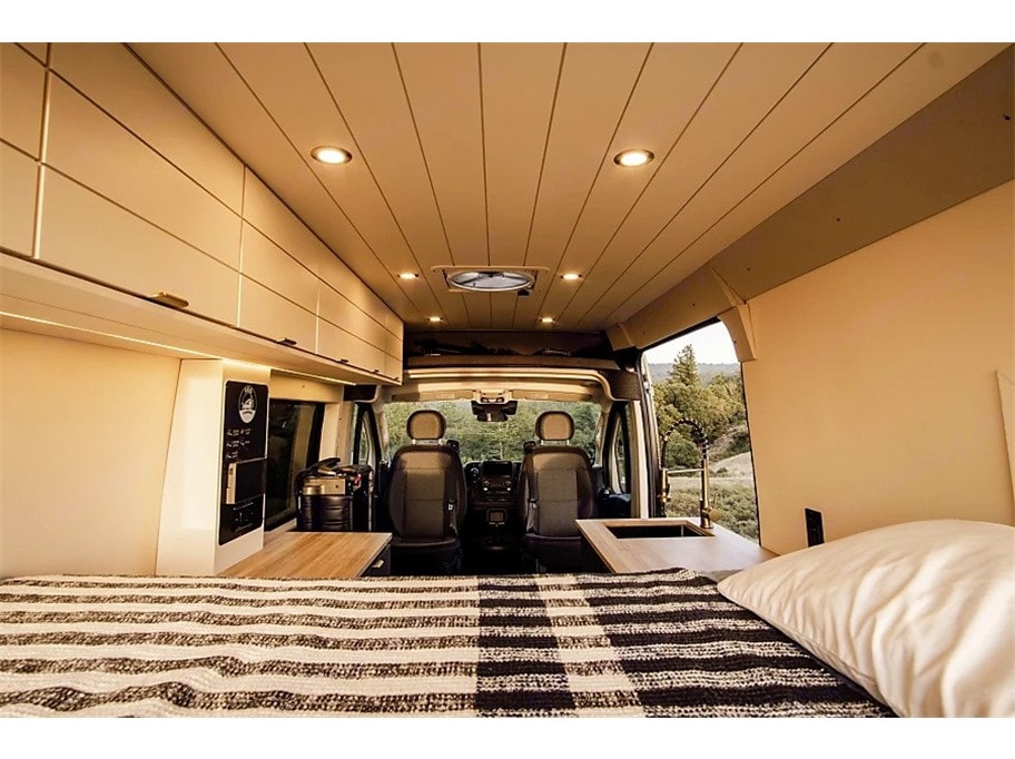 RV rental interior: A cozy camper van features a bed, kitchenette, and driver's cabin, perfect for travel adventures.. Dodge Ram Promaster 2023