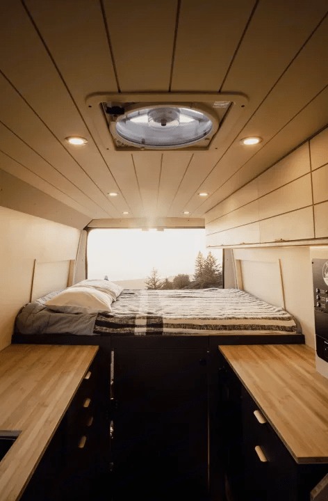 Cozy campervan rv rental interior: elevated bed with nature views, wood-paneled ceiling, fan, and compact kitchenettes.. Dodge Ram Promaster 2023