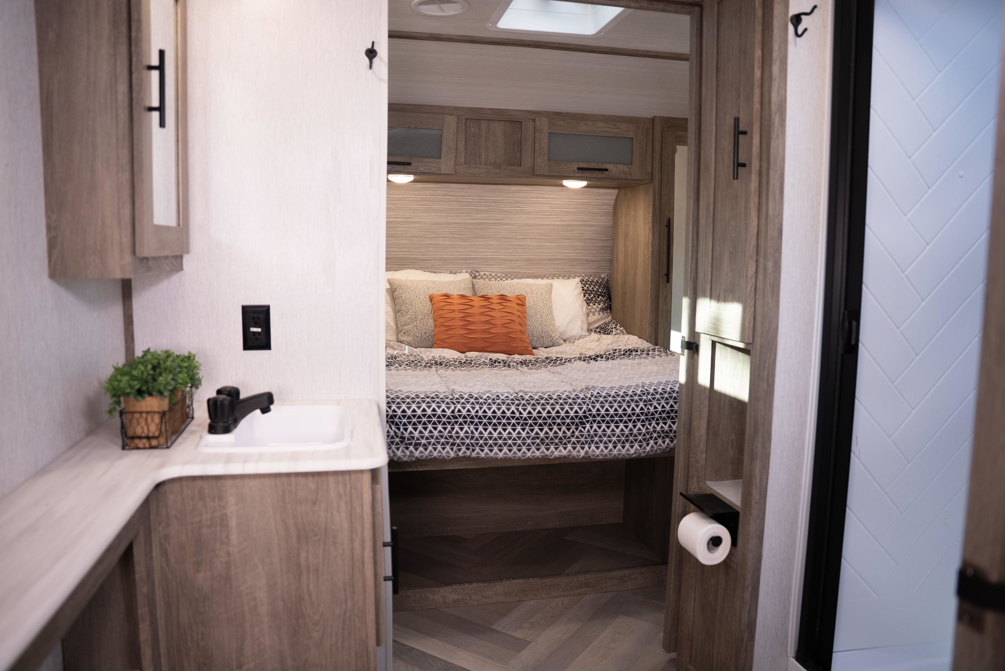 RV rental interior: A comfortable bedroom, adjacent vanity sink with greenery, and a hint of a modern bathroom. Ready for adventure.. Forest River Wildwood Heritage Glen 2022