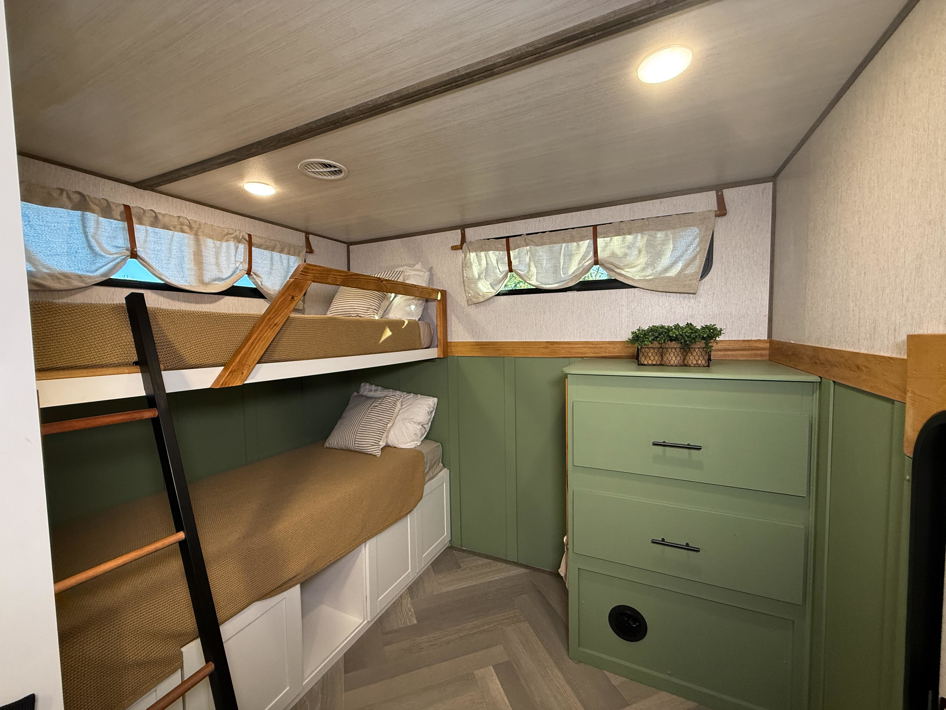 Cozy rv rental interior: bunk beds with wooden frame, brown blankets, green dresser, and wainscoting. Ideal for family trips.. Forest River Wildwood Heritage Glen 2022