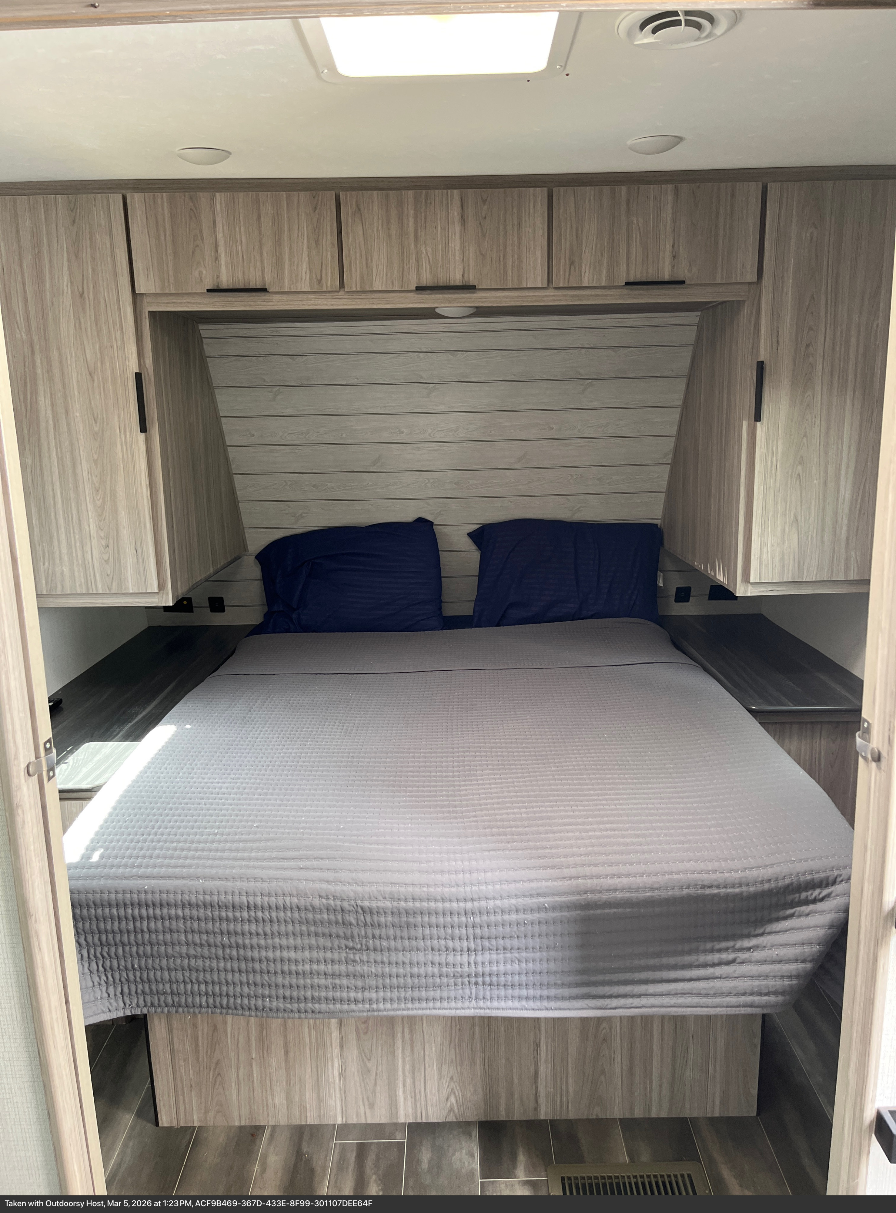 RV rental bedroom with bed, side shelves, overhead storage, and wood-paneled walls, perfect for a restful sleep on the road.. Keystone RV Passport SL 2021