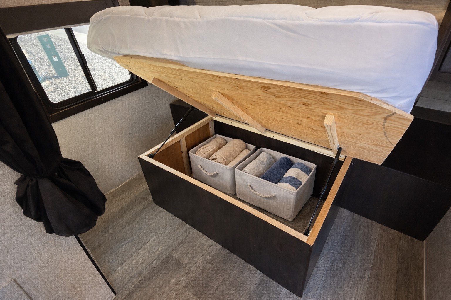 RV rental bed lifts to reveal under-bed storage with neatly folded towels in bins. Perfect for organized travel.. Jayco Jay Flight 2022