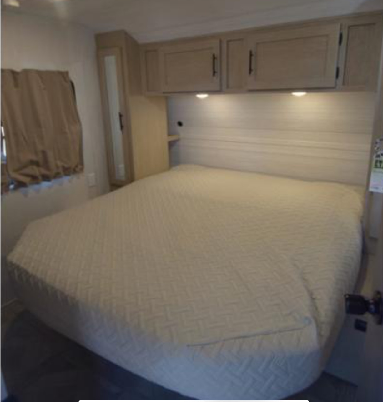 RV rental bedroom with a comfortable bed, overhead cabinets, and a window with curtains, offering a cozy sleeping area.. Forest River Salem Cruise Lite 2024
