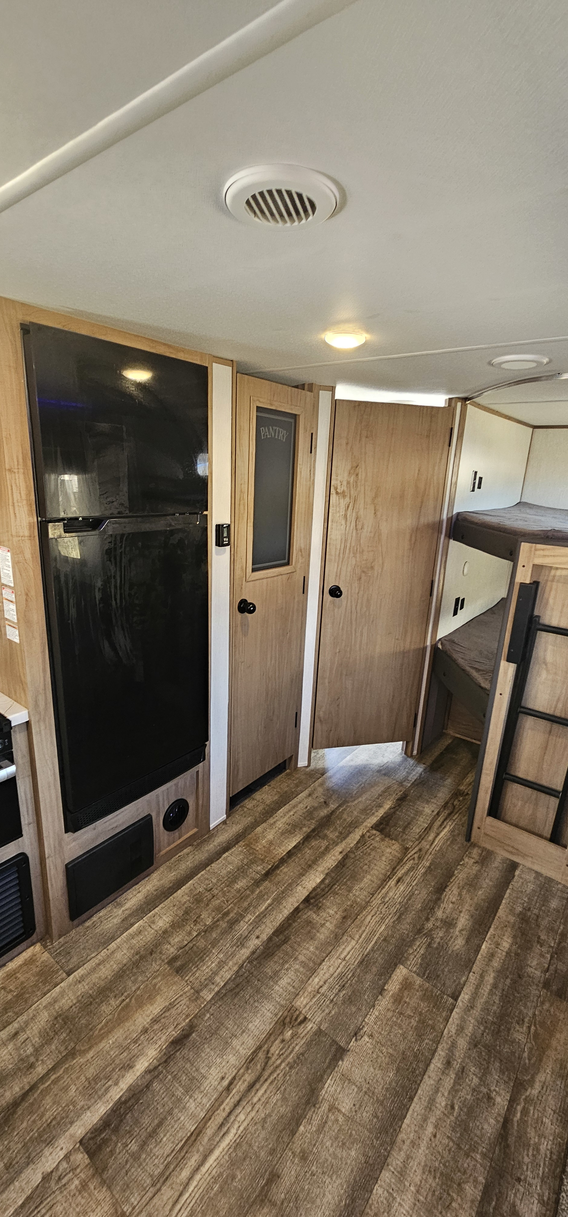 RV rental interior: fridge, pantry door, and bunk beds visible. Wood-look floor & ceiling vents complete this cozy living space.. Forest River Cherokee Alpha Wolf 2023