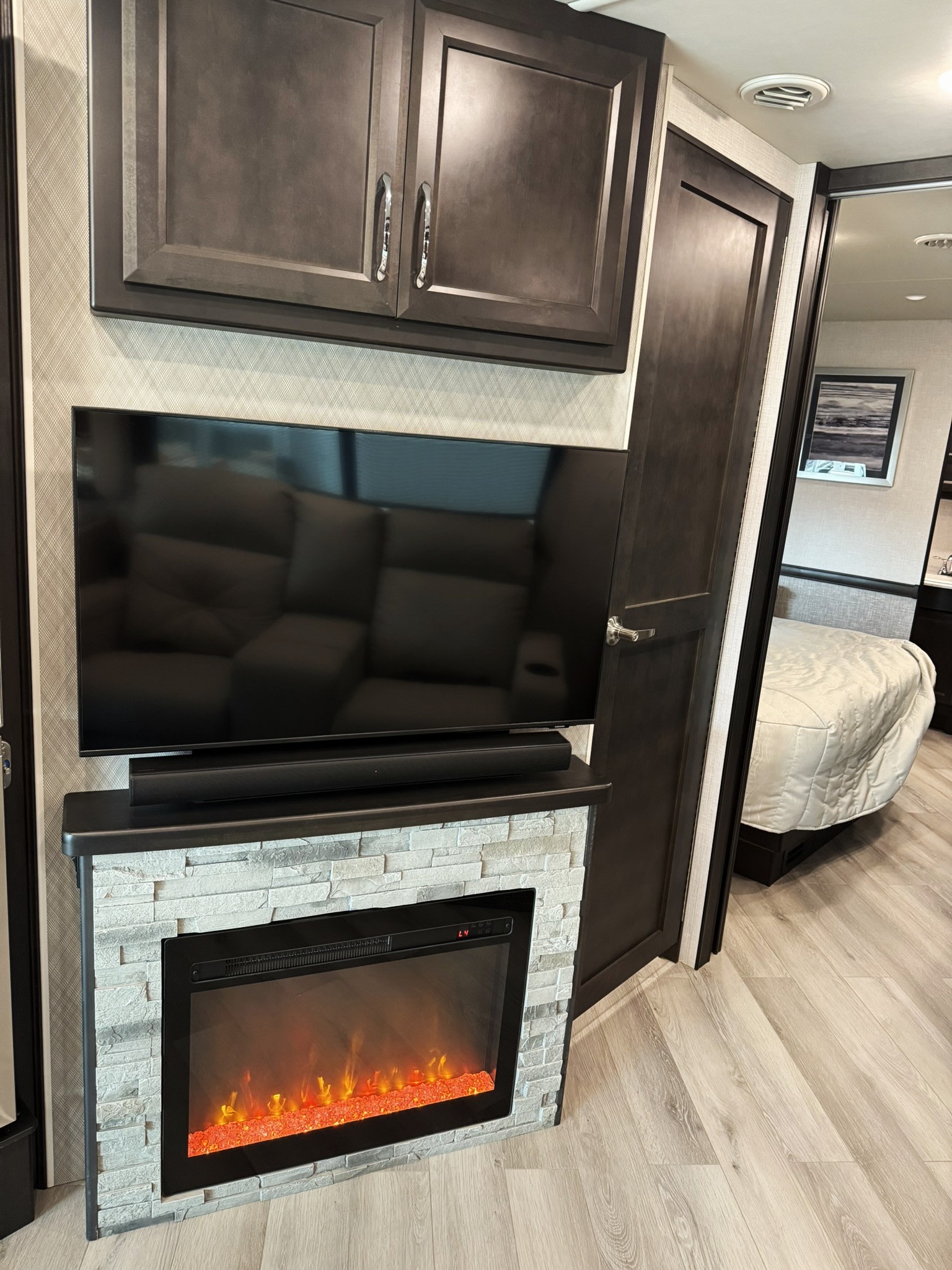 Enjoy an RV rental's cozy living area with an integrated TV, soundbar, and electric fireplace, plus a bedroom beyond.. Bounder Bounder Motorhome 2024