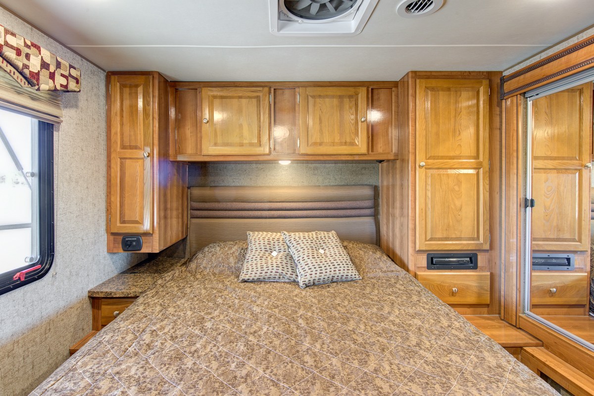 Cozy RV rental bedroom featuring a comfy bed, ample wood cabinetry, and a mirrored closet for storage.. Forest River Coachmen Leprechaun 2016
