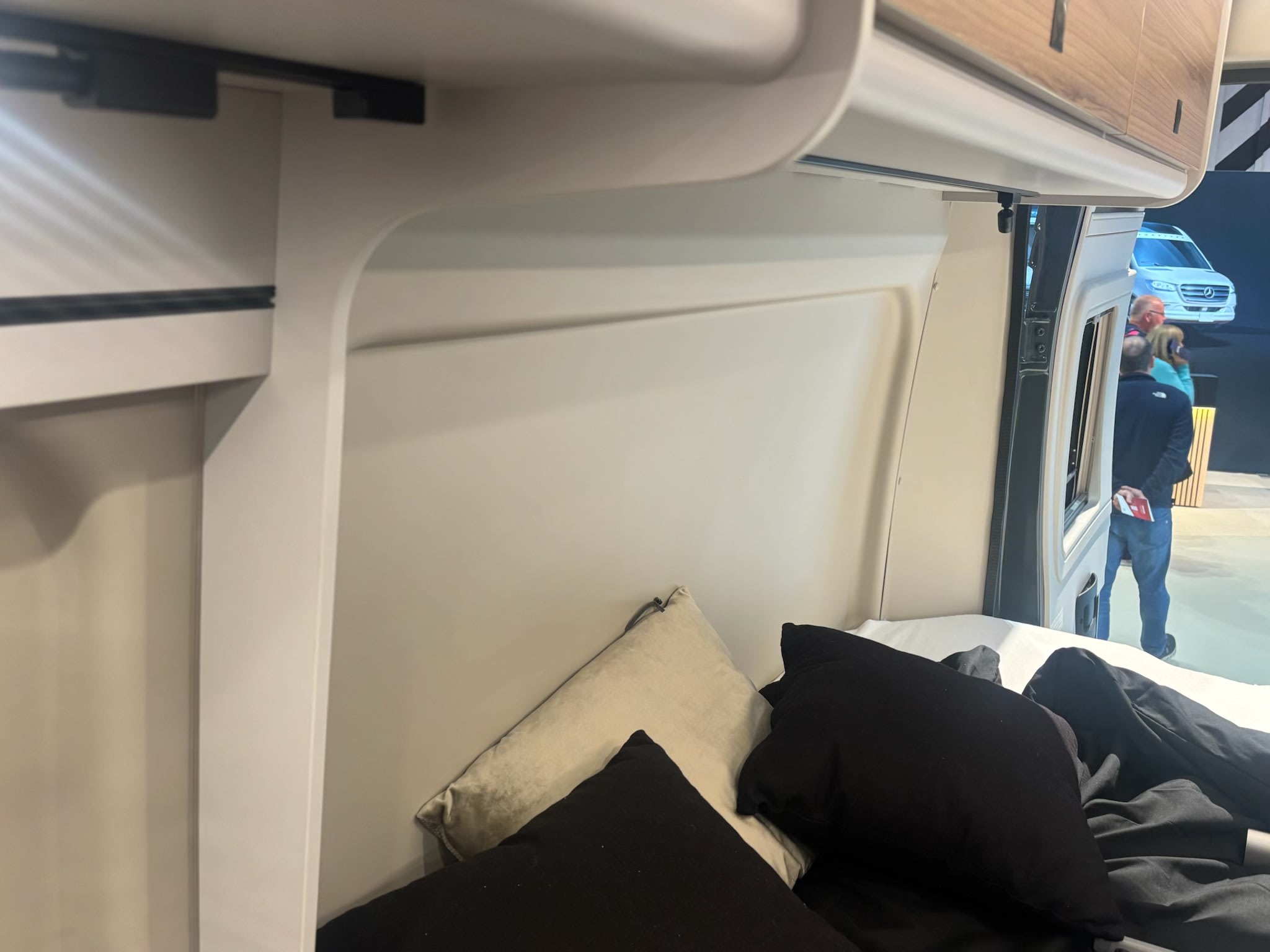 RV rental interior: Comfortable bed with pillows, overhead cabinets, and an outside view of a white camper van.. Burstner B66 2026