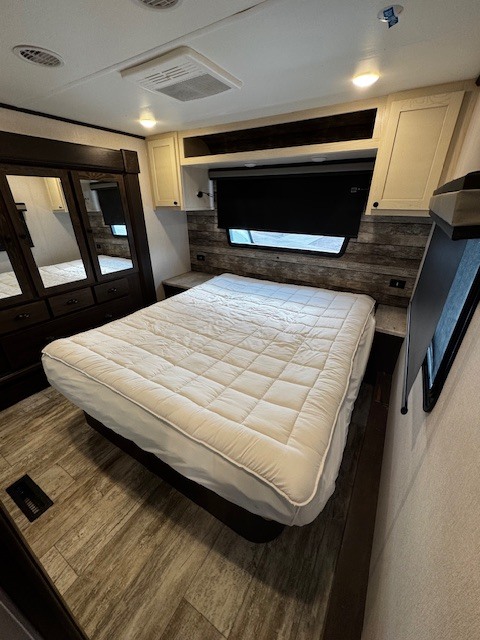 Spacious RV rental bedroom featuring a queen bed, mirrored dresser, and modern overhead cabinetry. Ready for your travels.. Forest River XLR Nitro Toy Hauler 2022
