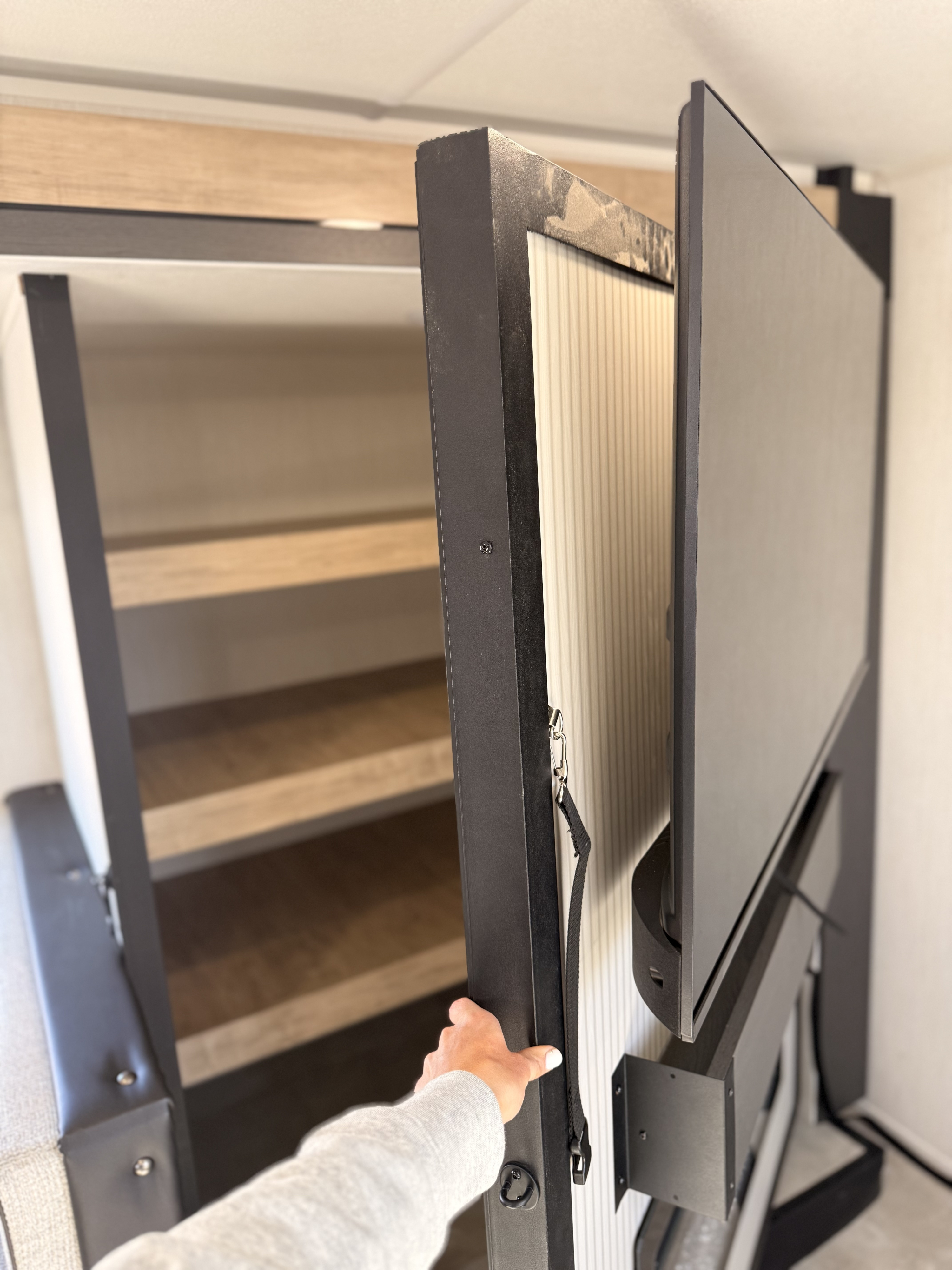 RV rental: A hand opens a black panel, revealing a TV mounted on it and shelves for compact storage inside.. Forest River Campsite Reserve 2026