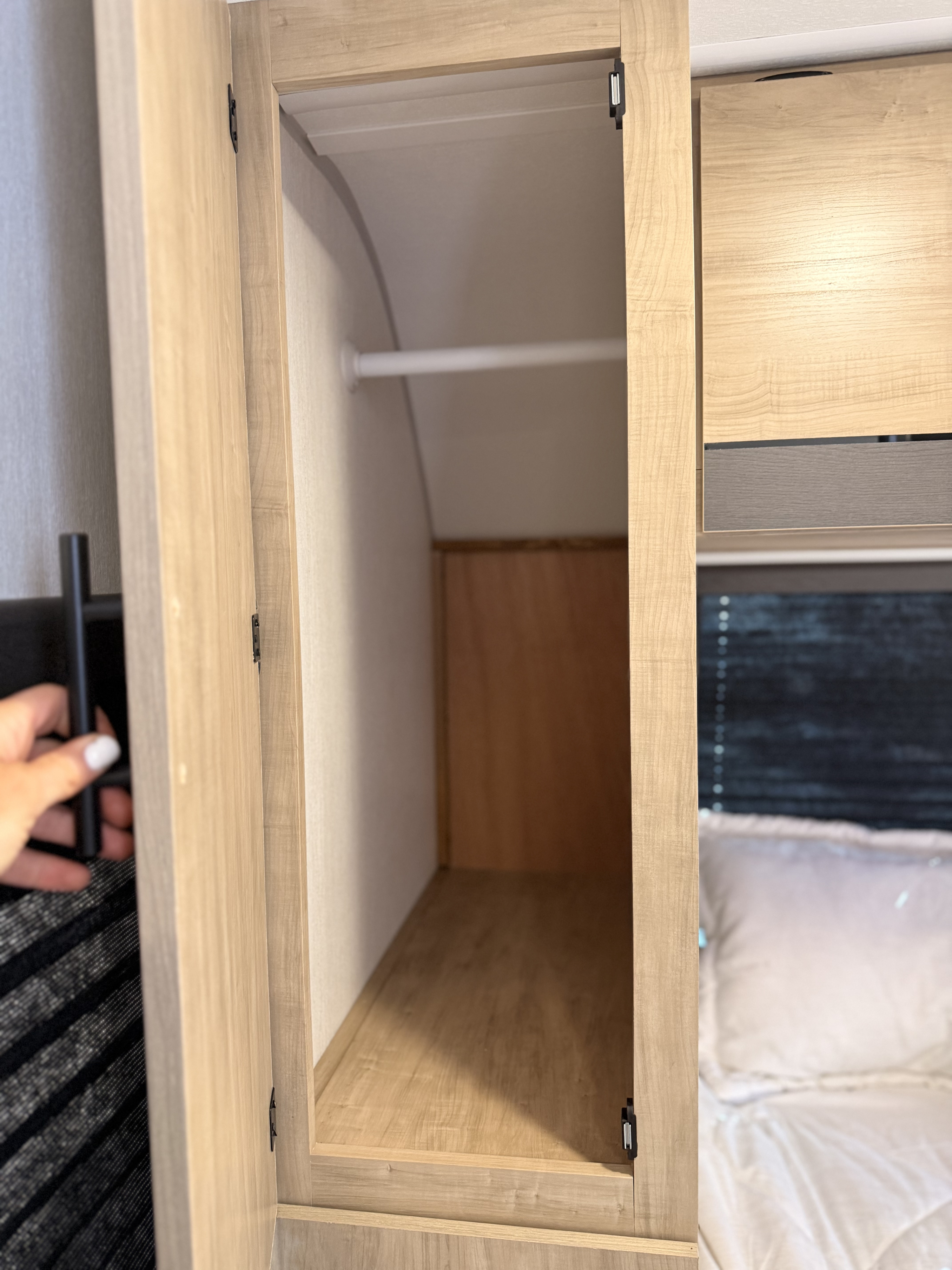 Exploring storage in an rv rental: This light wood closet is open, showing a hanging rod & arched back. Bed visible right.. Forest River Campsite Reserve 2026
