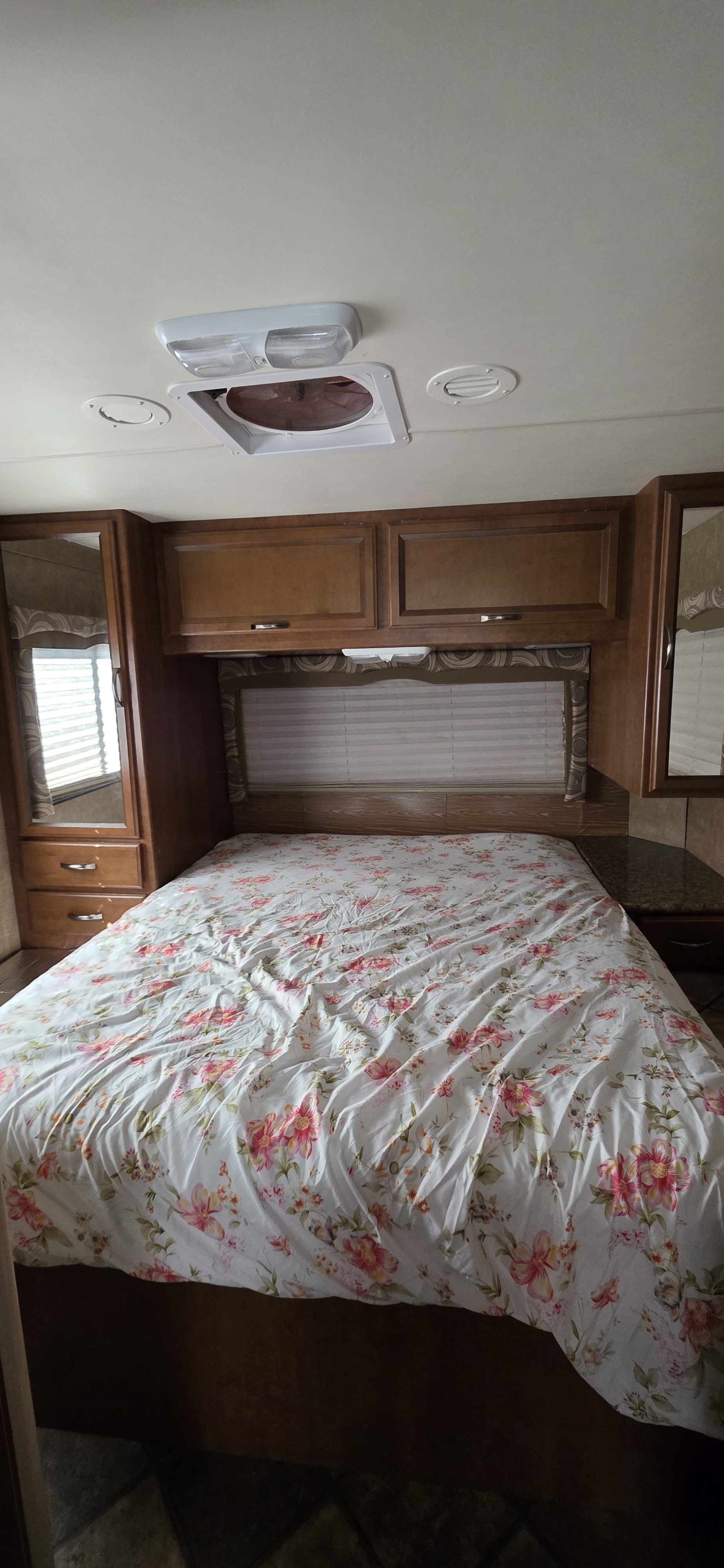 This RV rental bedroom features a floral bedspread, wood cabinets, side mirrors, and ceiling fan. Cozy interior for travel.. Thor Chateau 2014