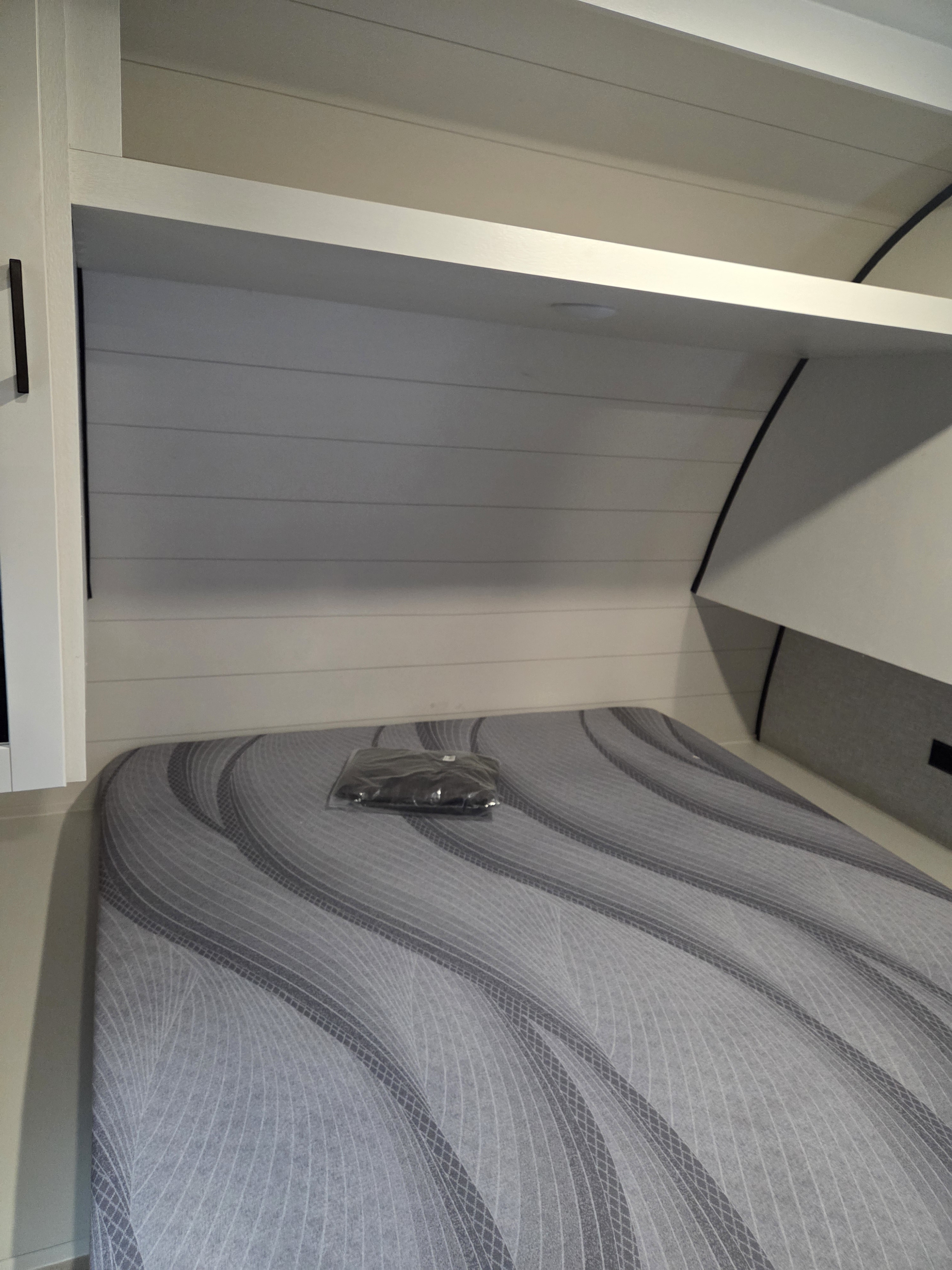 A clean RV rental bedroom features a gray patterned bed, white shiplap headboard, and an overhead shelf for storage.. Open Range Conventional 26BHS Travel Trailer 2025