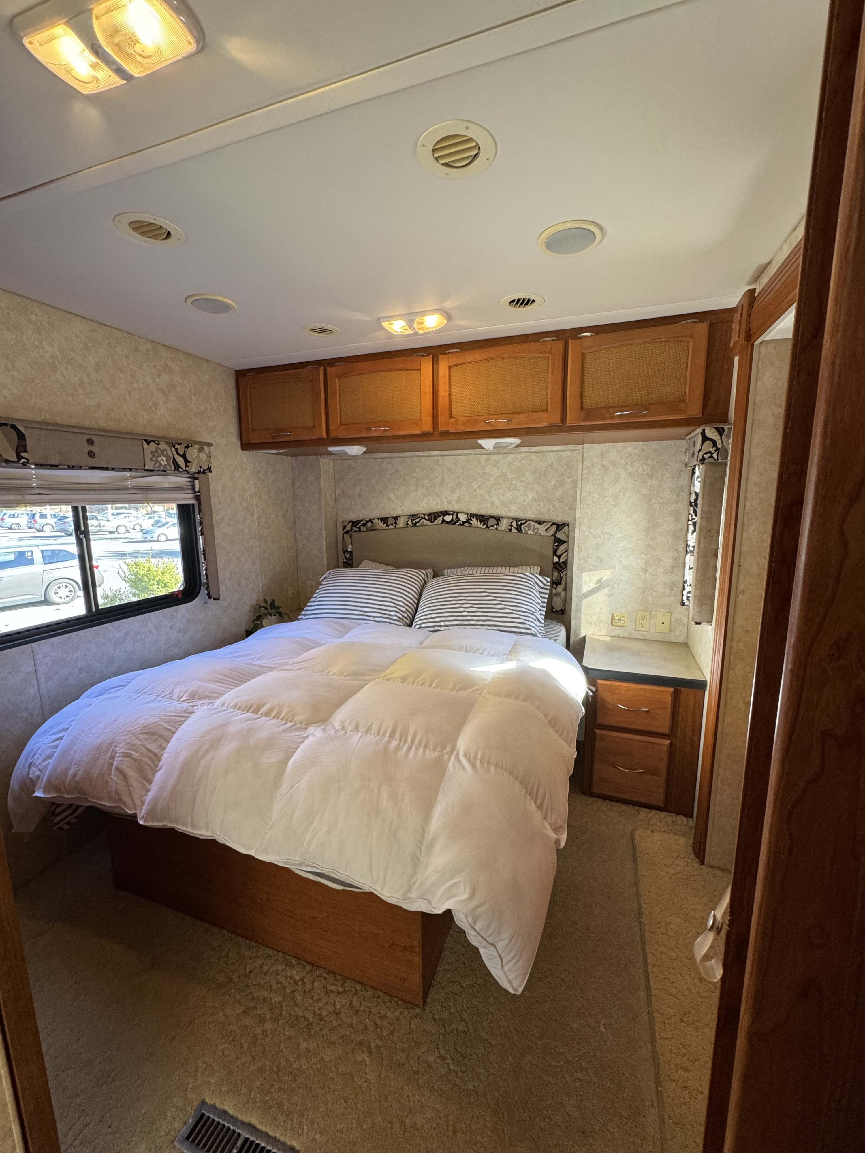 Comfortable RV rental bedroom features a large bed, overhead storage, nightstand, and window view for a relaxing stay.. Safari Simba 2006