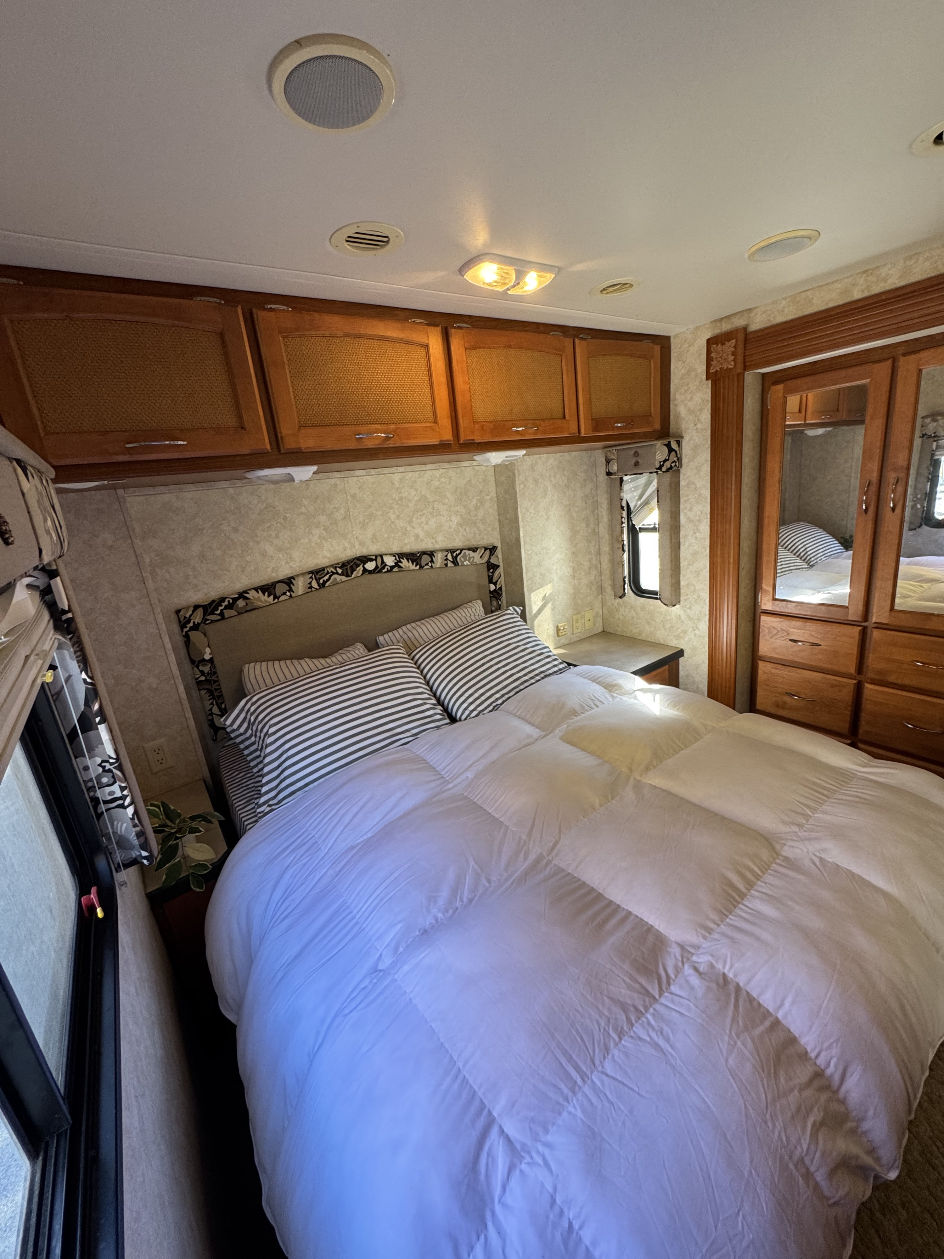 Cozy rv rental bedroom with a comfortable bed, white comforter, striped pillows, overhead cabinets, and mirrored wardrobe.. Safari Simba 2006