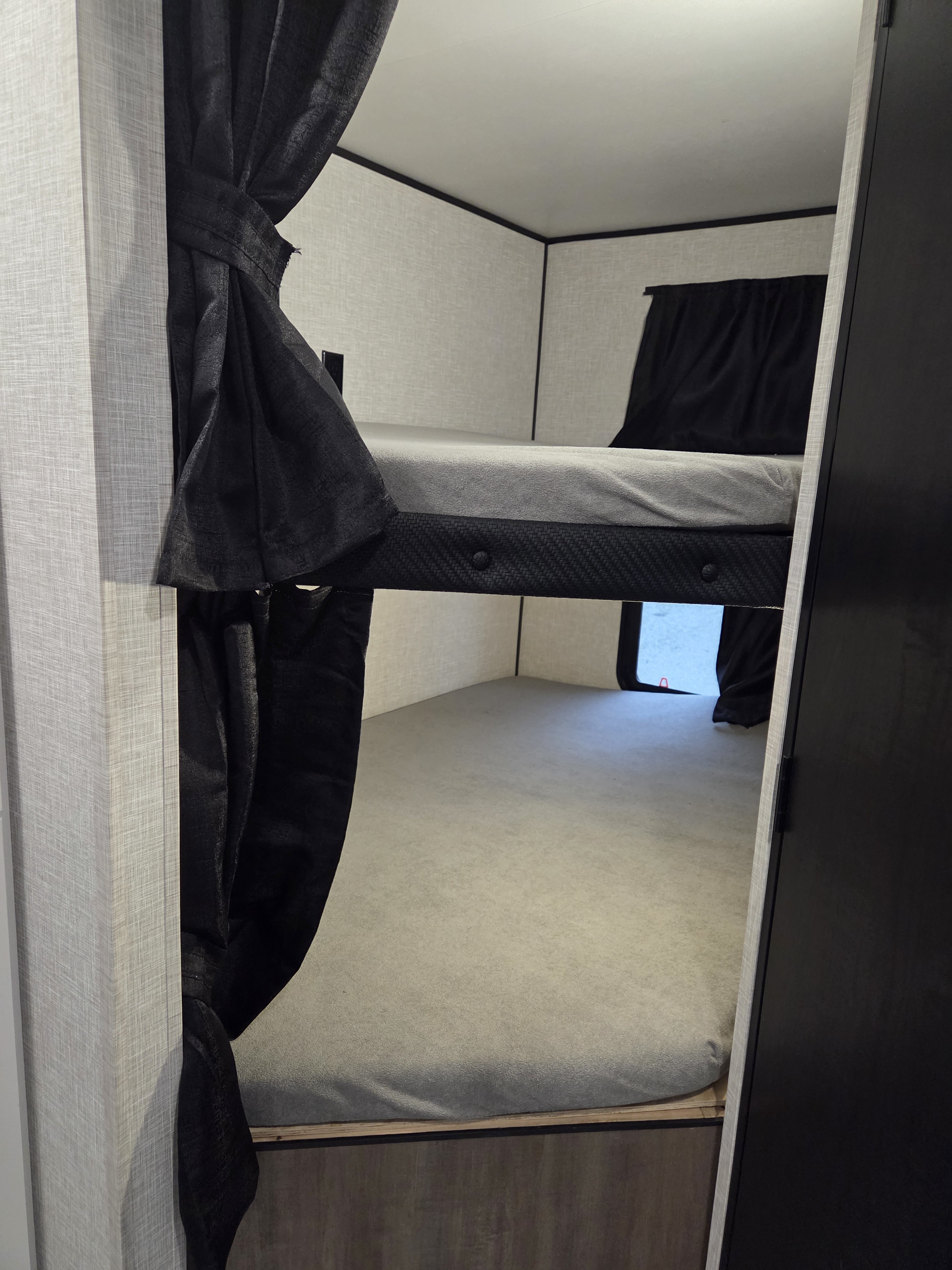Interior of an RV rental showing stacked bunk beds with light gray mattresses and tied black privacy curtains. A window is visible on the lower bunk.. Open Range Conventional 26BHS Travel Trailer 2025