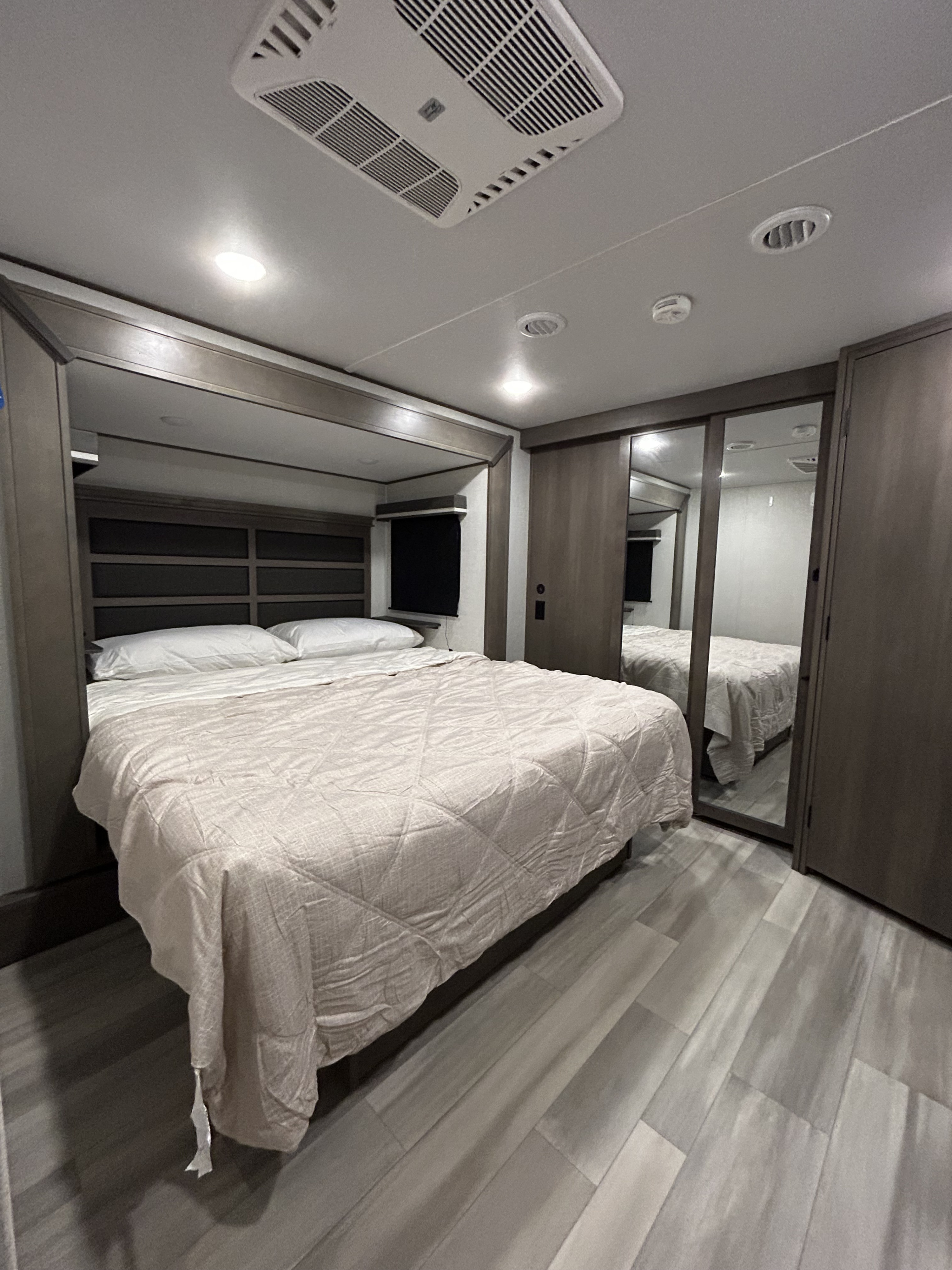 Spacious RV rental bedroom featuring a comfy queen bed, mirrored closet, and modern ceiling AC/lighting for your next adventure.. Grand Design Solitude 2023