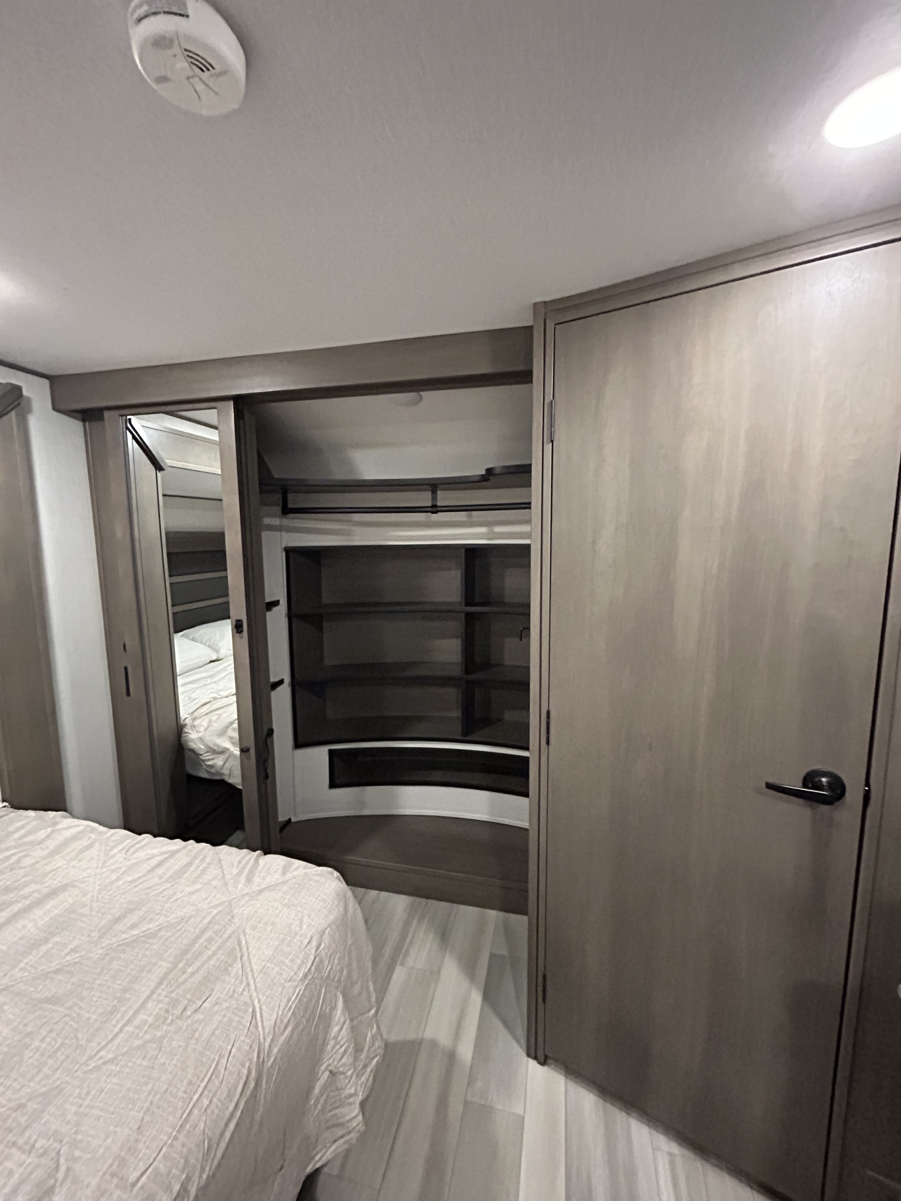 RV rental bedroom with a bed, sliding mirrored closet, built-in shelving, and wood-look flooring.. Grand Design Solitude 2023
