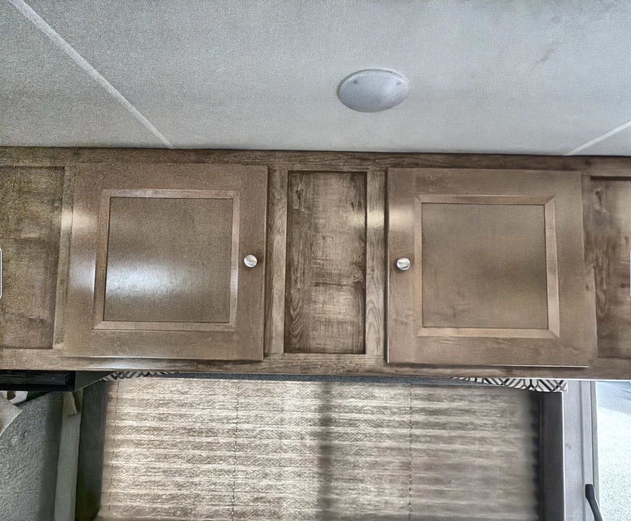 RV rental interior featuring wooden overhead cabinets, a ceiling light, and pleated window blinds.. Coachman Leprachaun 2020