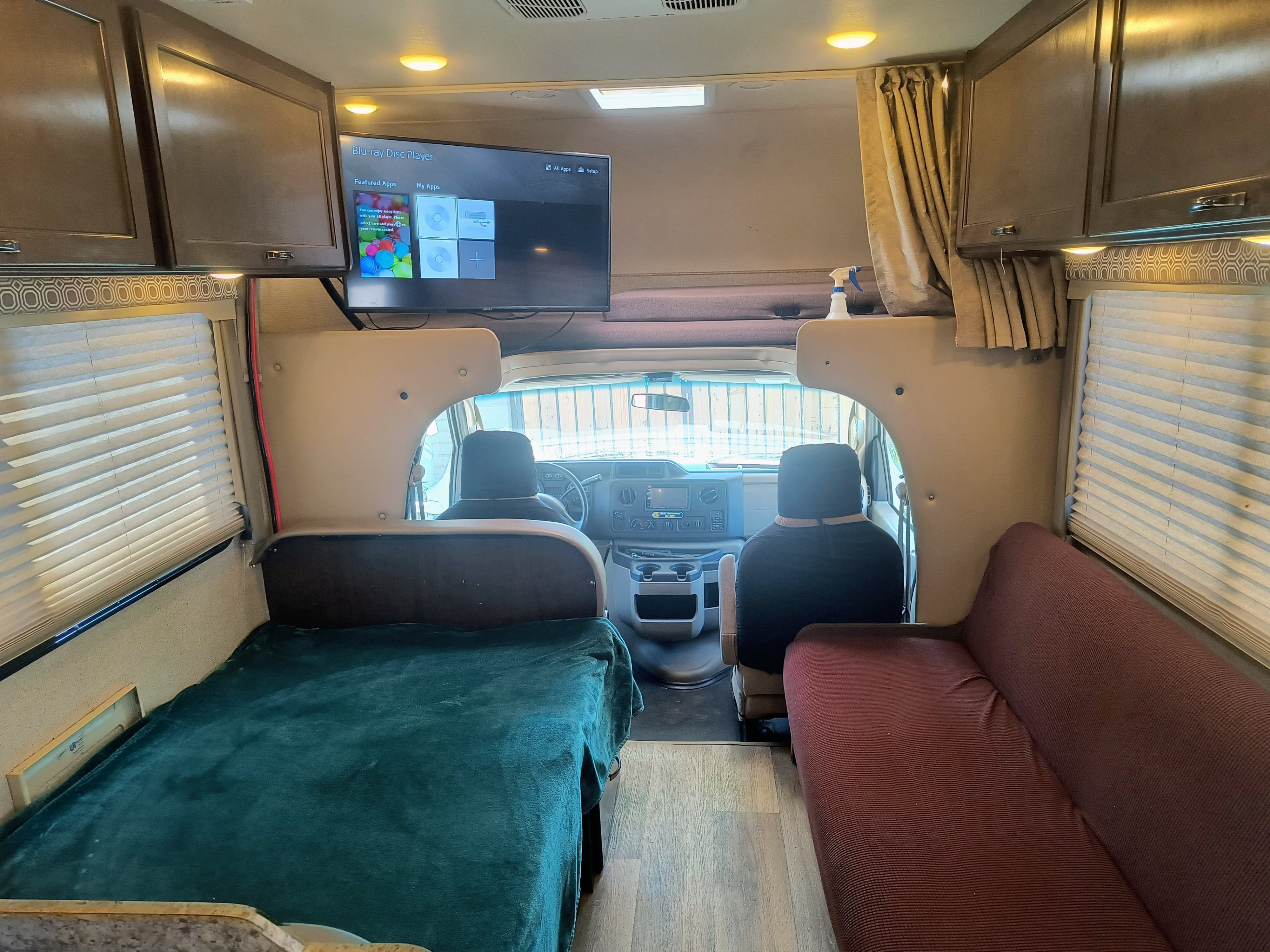 This RV rental interior features a TV with Blu-ray apps, a cozy bed, a sofa, and the front cockpit area, ideal for travel.. Thor Motor Coach Four Winds 2017