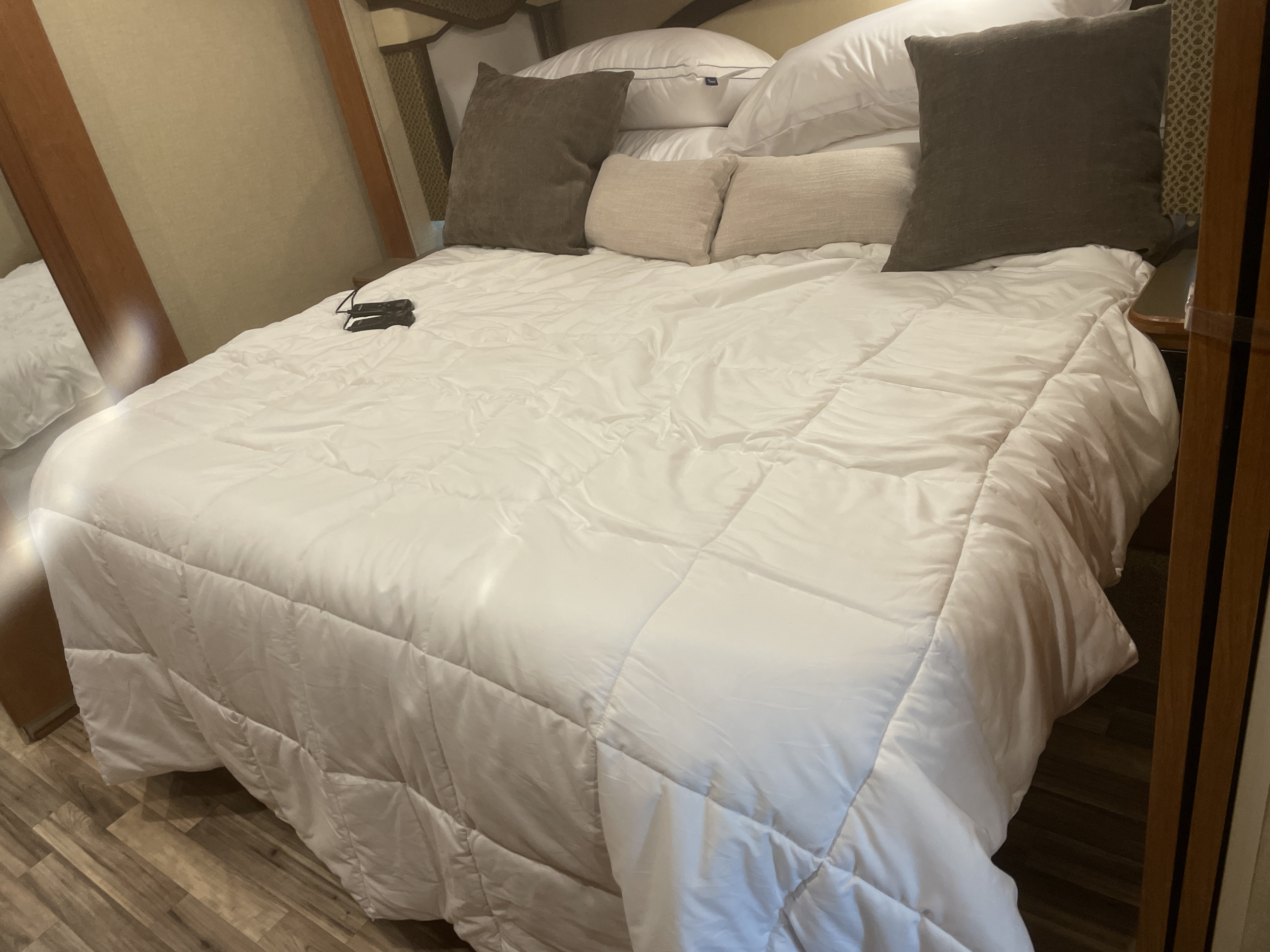 Comfortable bed in an RV rental bedroom, featuring a pristine white comforter, plush pillows, and wooden accents.. Winnebago Sunova 2017