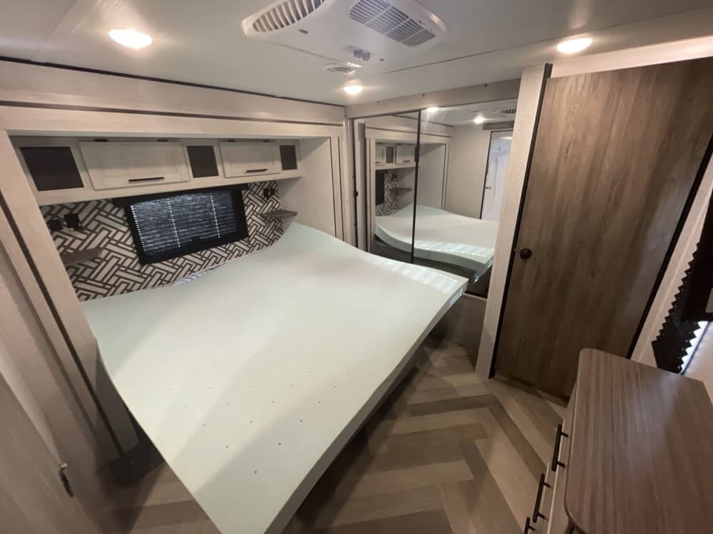 Experience this RV rental bedroom: a modern space with a comfy bed, geometric wall accent, overhead storage, and mirrored closet.. Crossroads RV Zinger 2024