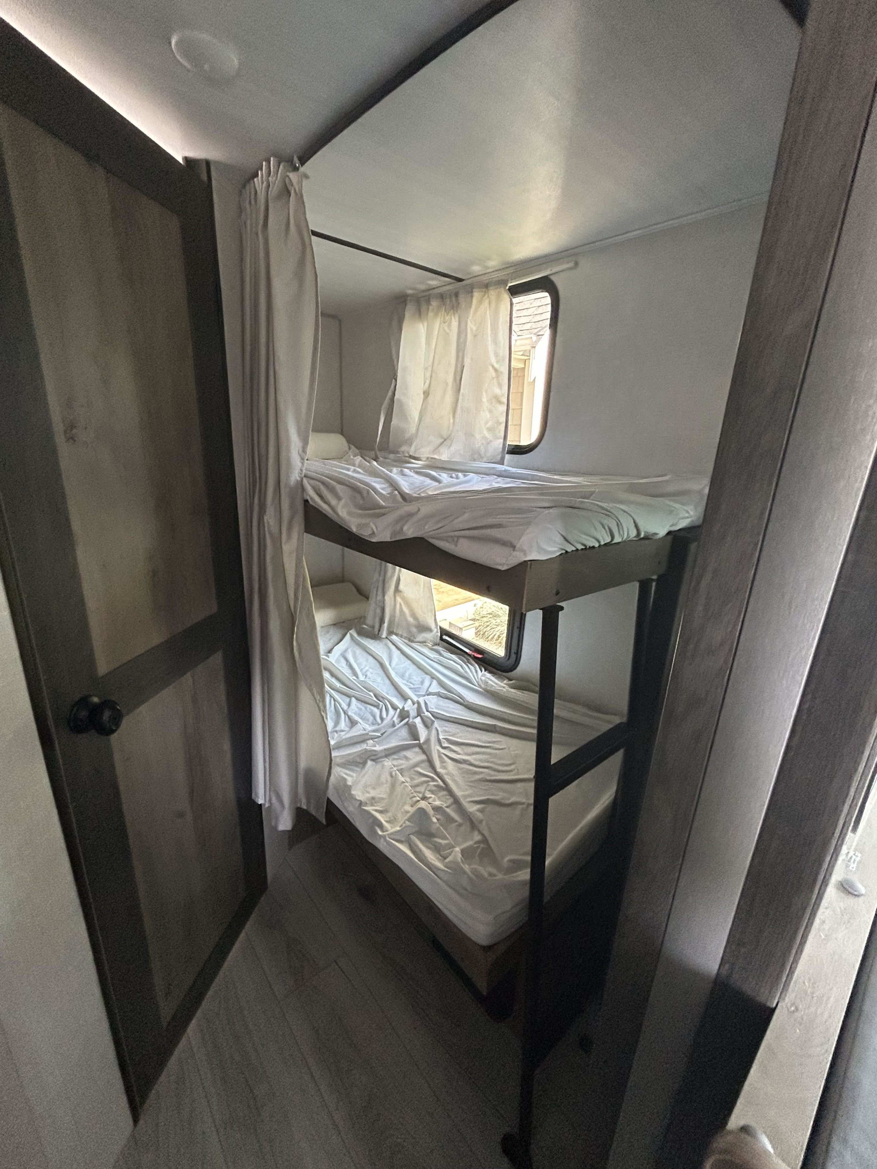 Inside an RV rental: a compact sleeping area with two bunk beds, white linens, privacy curtains, and a window.. Forest River Surveyor Legend 2022
