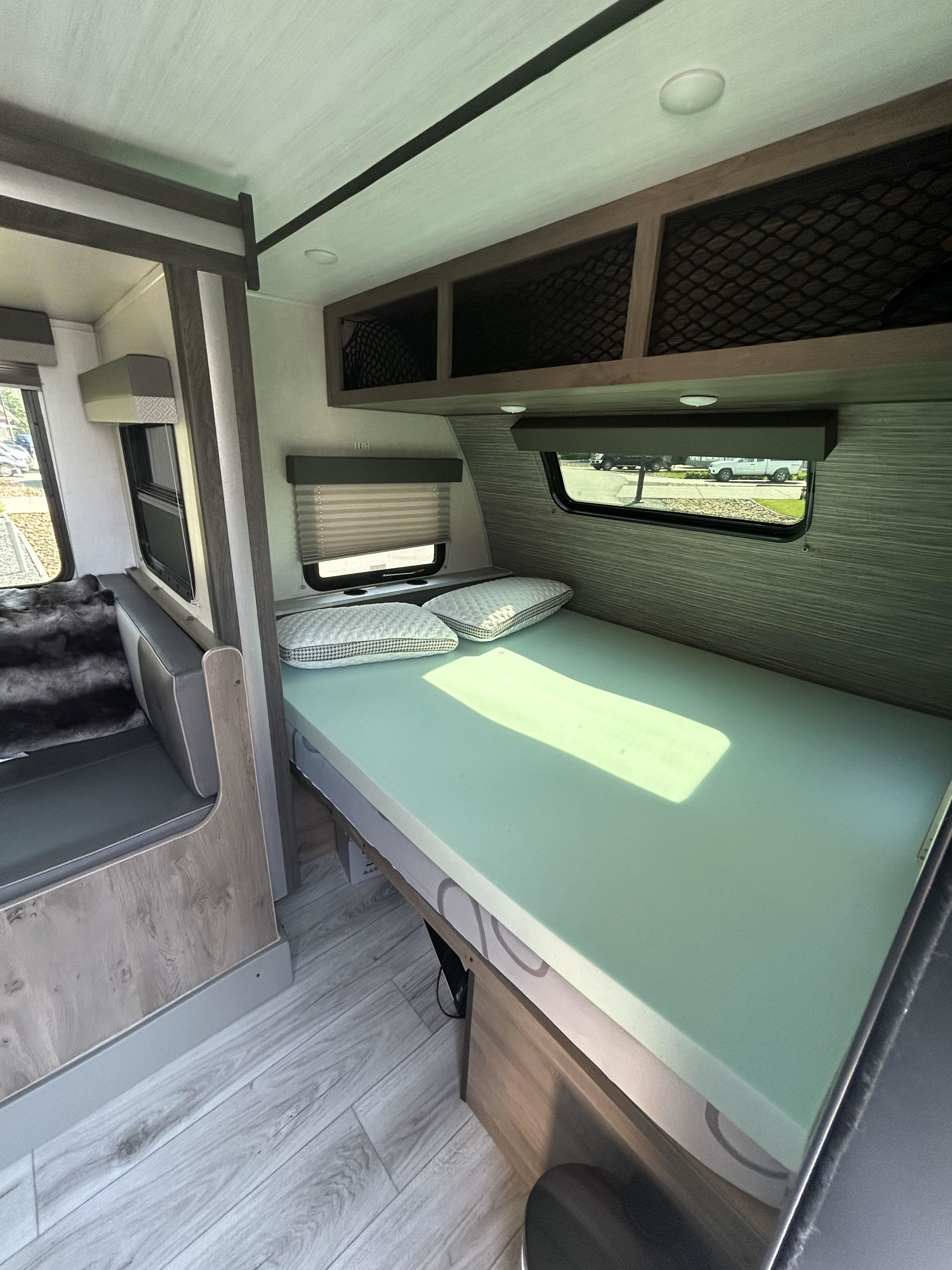 Modern RV rental interior featuring a bed, seating area, overhead storage, and windows. Ready for your next adventure!. Forest River Surveyor Legend 2022