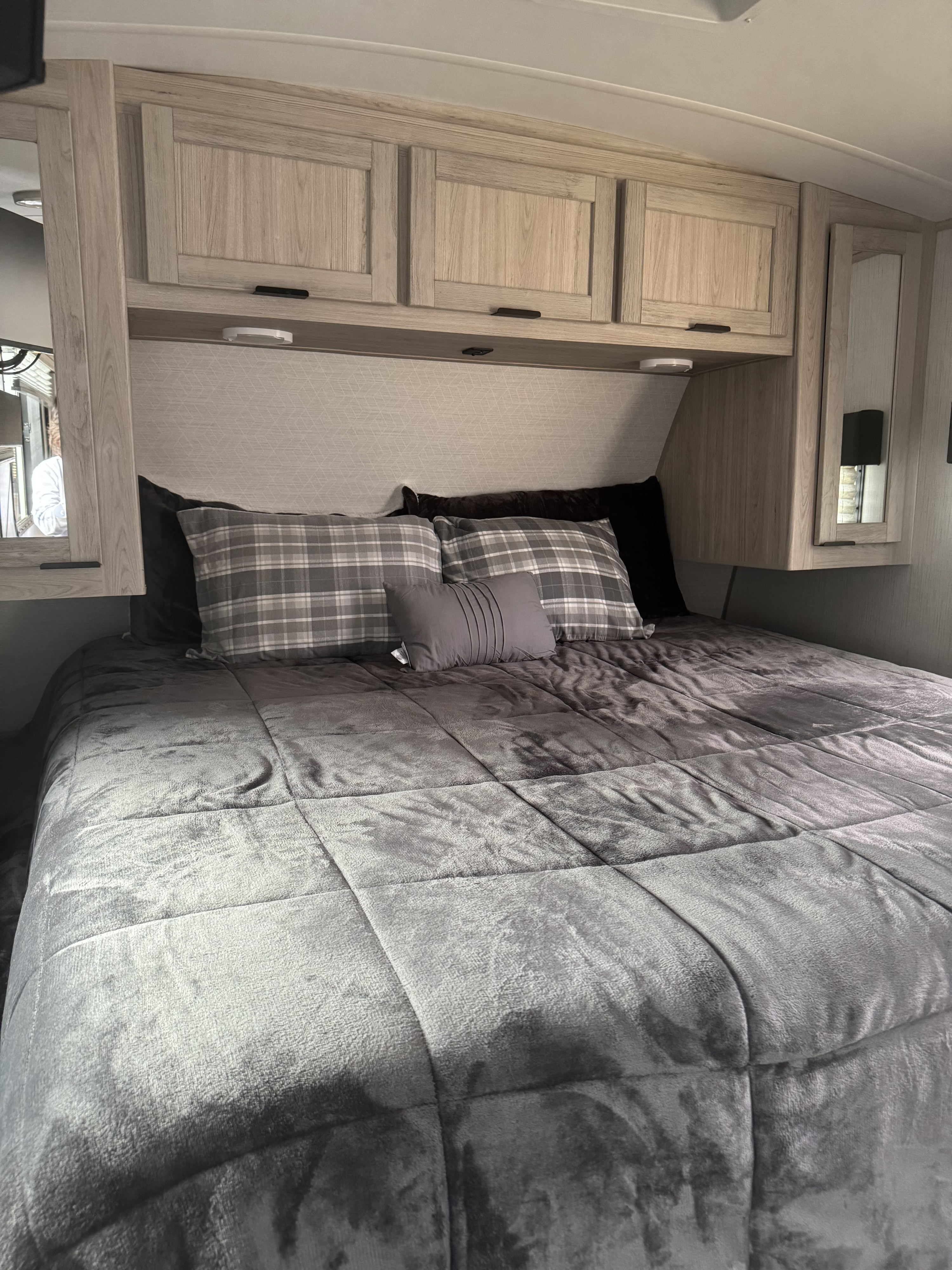 This RV rental's cozy bedroom features a grey bed, plaid pillows, and light wood overhead cabinets for storage.. Cruiser RV Shadow Cruiser 2022