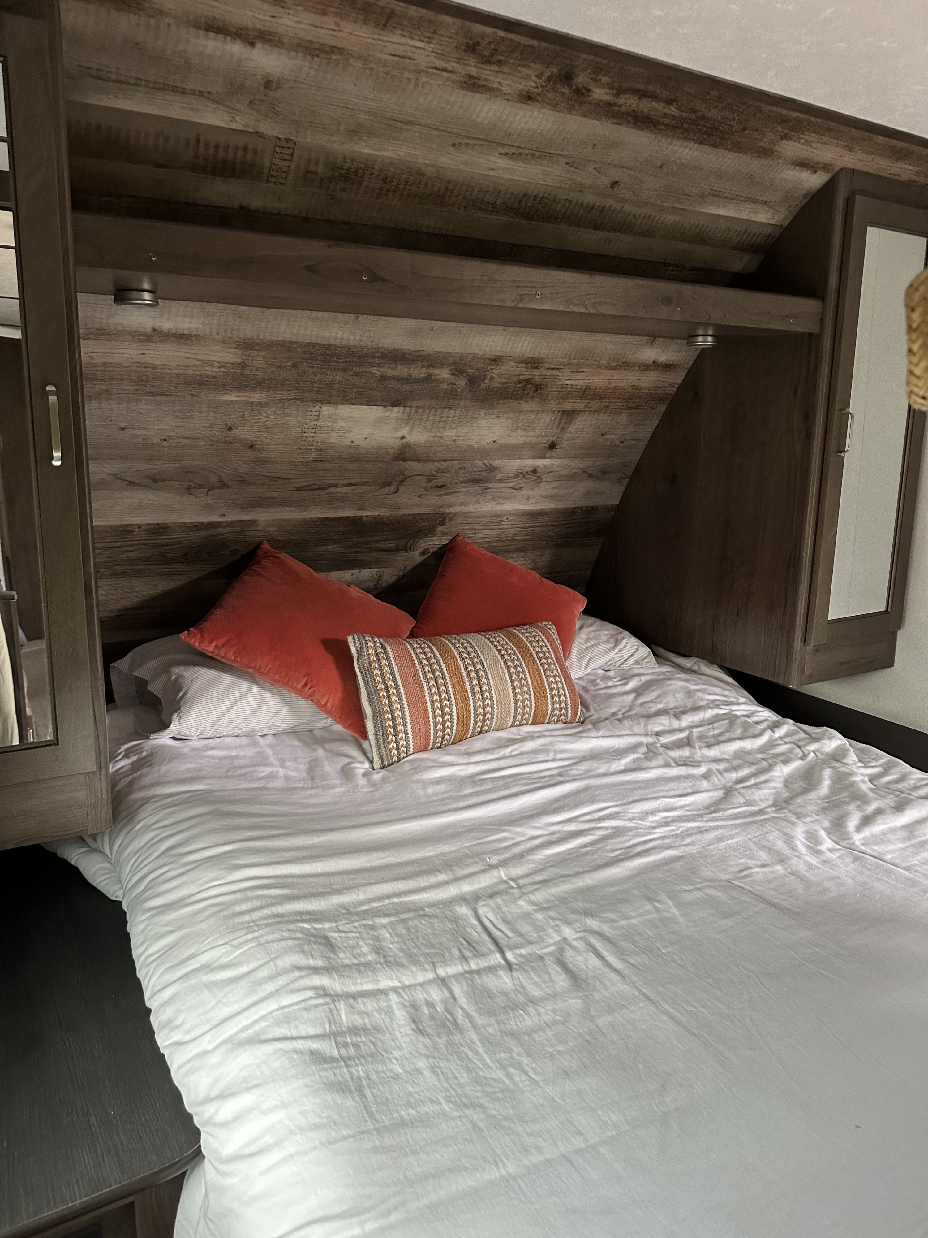 RV rental bedroom featuring a cozy bed with white sheets, orange and striped pillows, and a wood-look headboard.. Keystone RV Passport Ultra Lite 2019