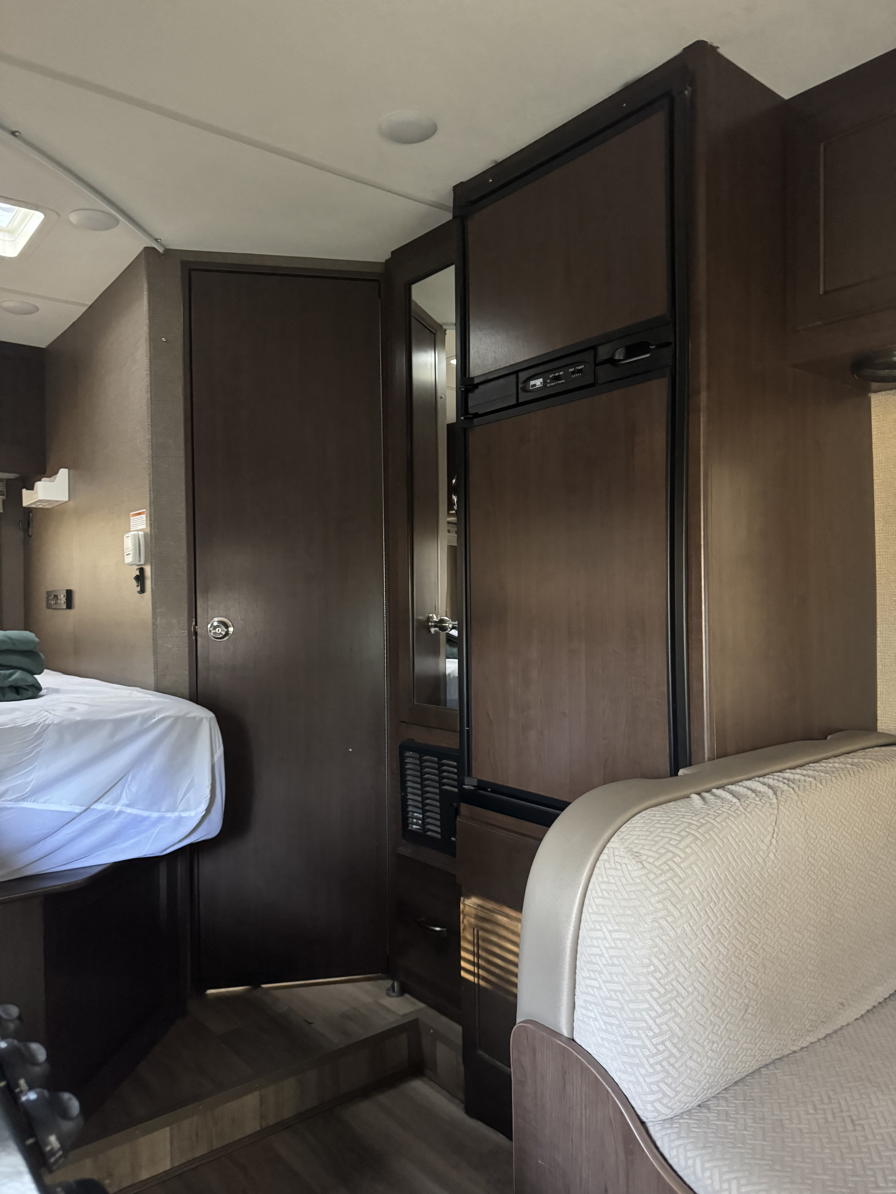 Interior of an rv rental featuring a bed, refrigerator, and dinette area, all within modern dark wood cabinetry.. Thor Four Winds 2017
