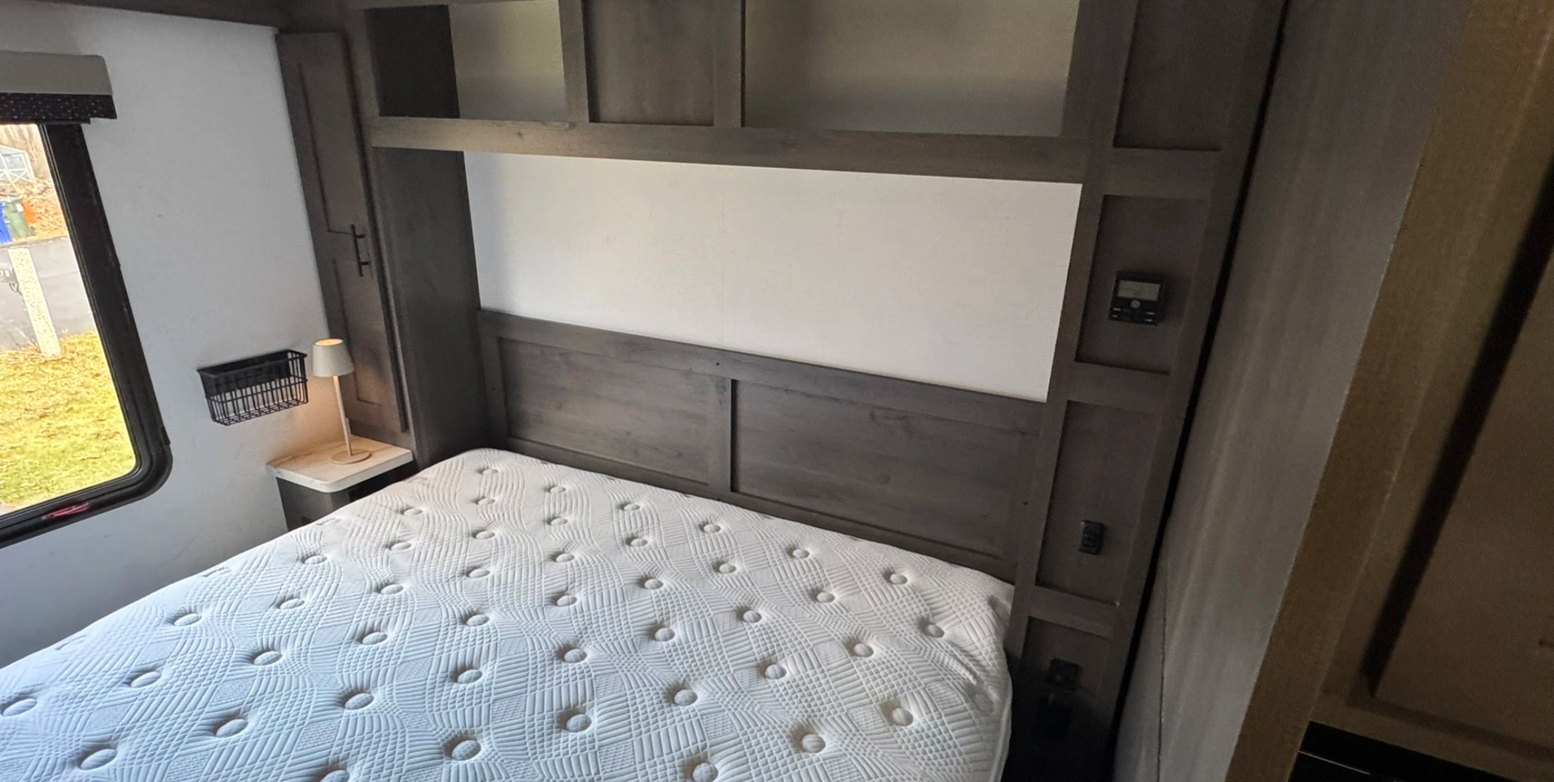 This RV rental bedroom features a white mattress, wooden headboard, side window, and built-in storage.. FR3 FR3 Motorhome 2023