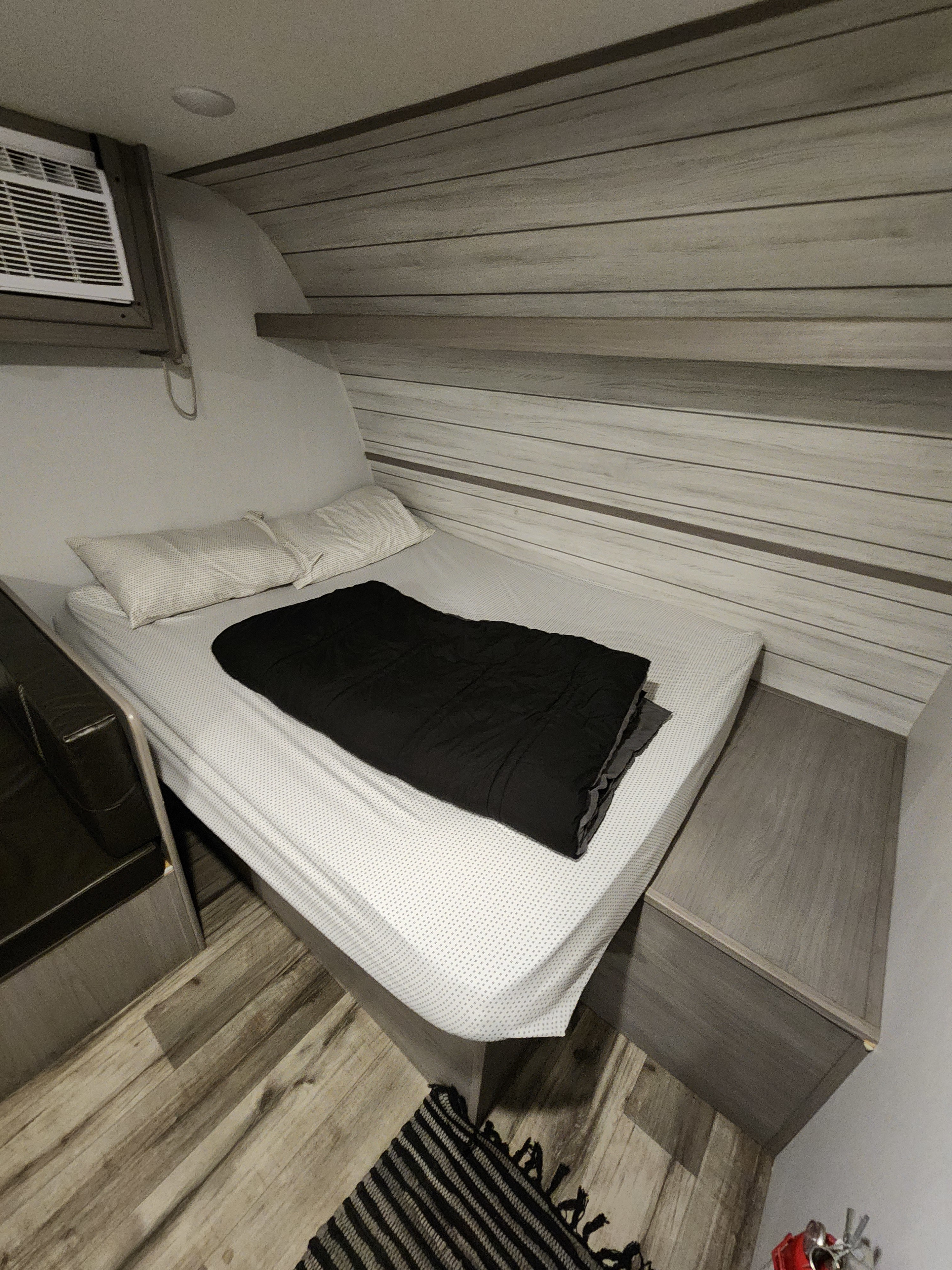 Cozy rv rental bedroom featuring a bed with white sheets, black comforter, overhead AC unit, and wood-paneled walls.. Dutchmen Coleman 2024