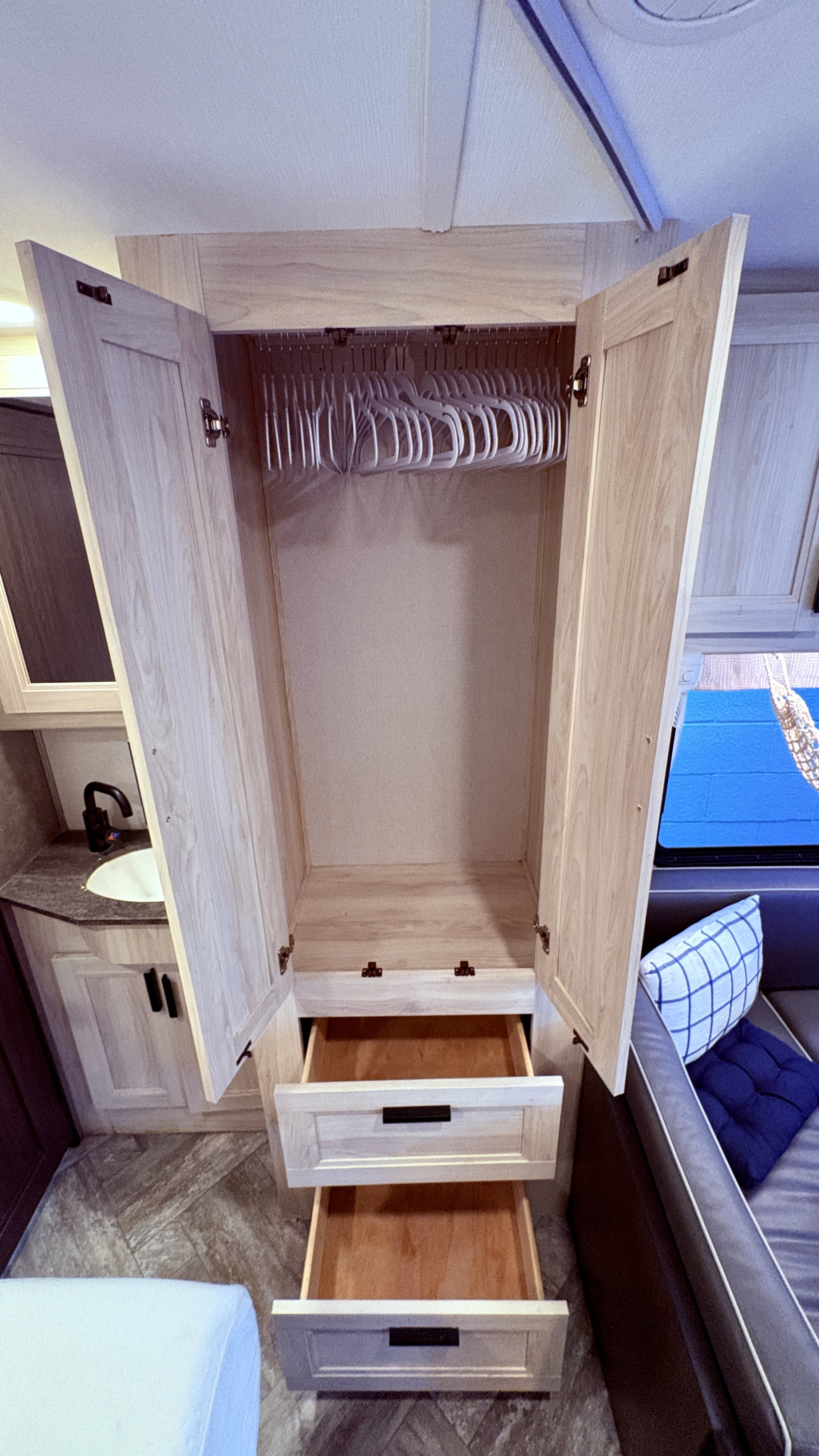 RV rental's compact interior: Light wood wardrobe with hangers, two open drawers, sink vanity, and sofa. Optimized storage.. Forest River Sunseeker LE 2023