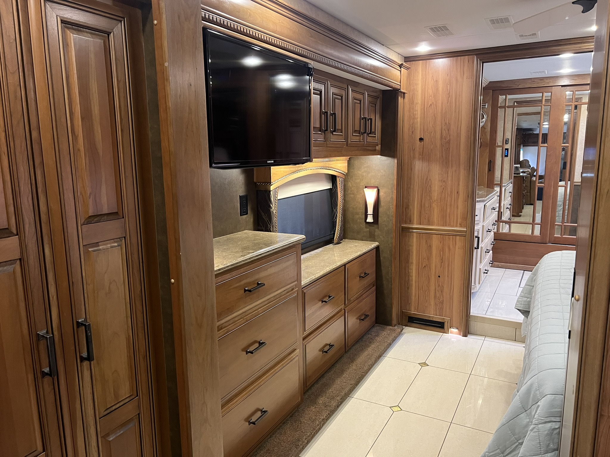 Luxurious RV rental bedroom featuring rich wood cabinets, TV, and stylish tile floors. Enjoy ample storage on your trip.. Entegra Coach Aspire 2015