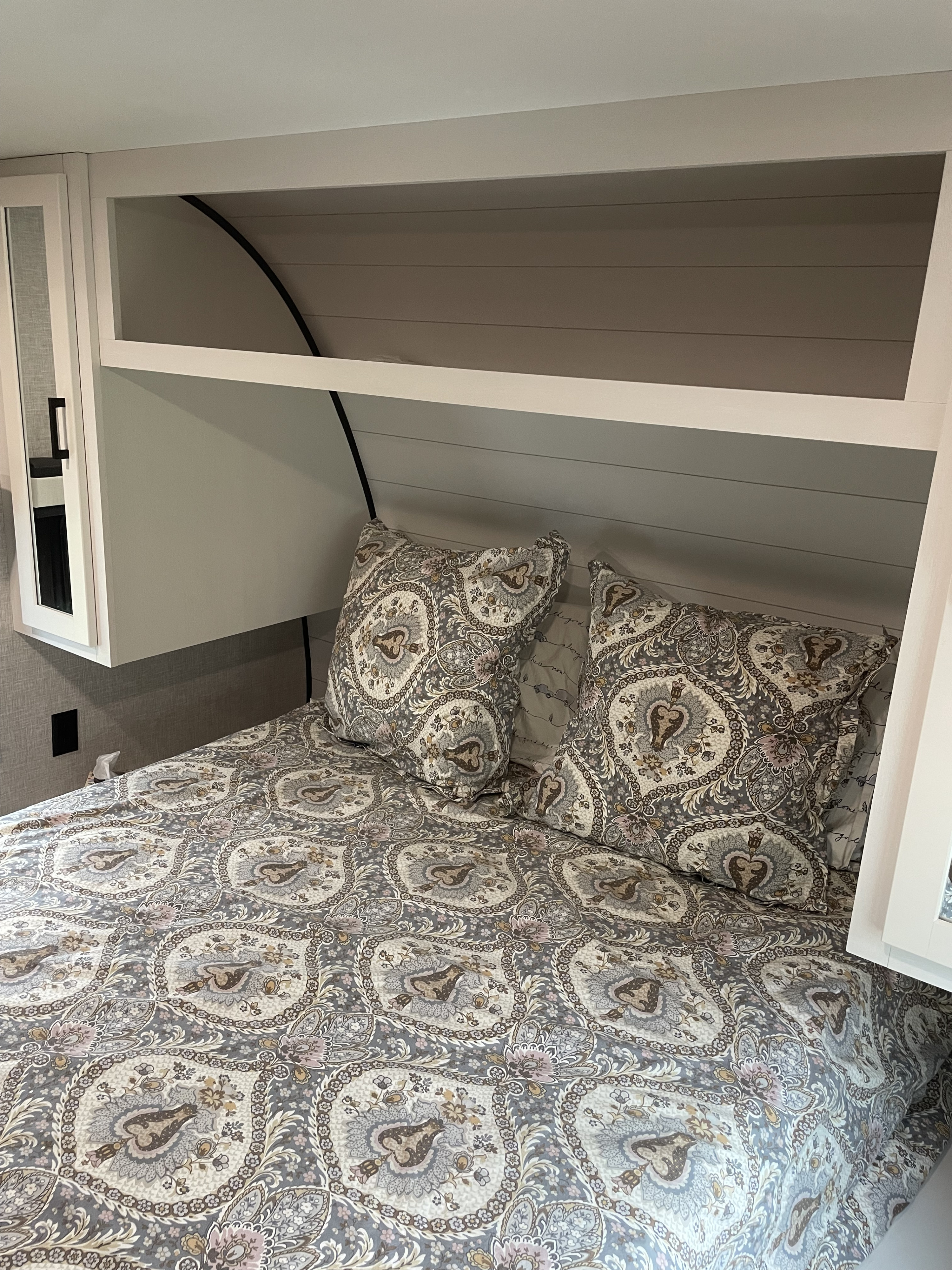 RV rental bedroom features a cozy bed with a gray and brown paisley comforter, pillows, and built-in storage.. Jayco Jay Flight 2024