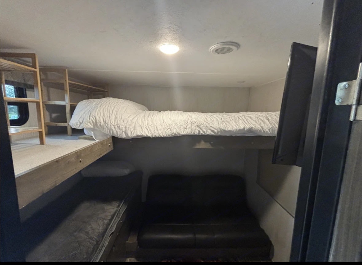 This RV rental bunk room offers an upper bed, a lower couch/bed, shelving, and a mounted TV in a compact space.. Forest River Palomino Puma 2021