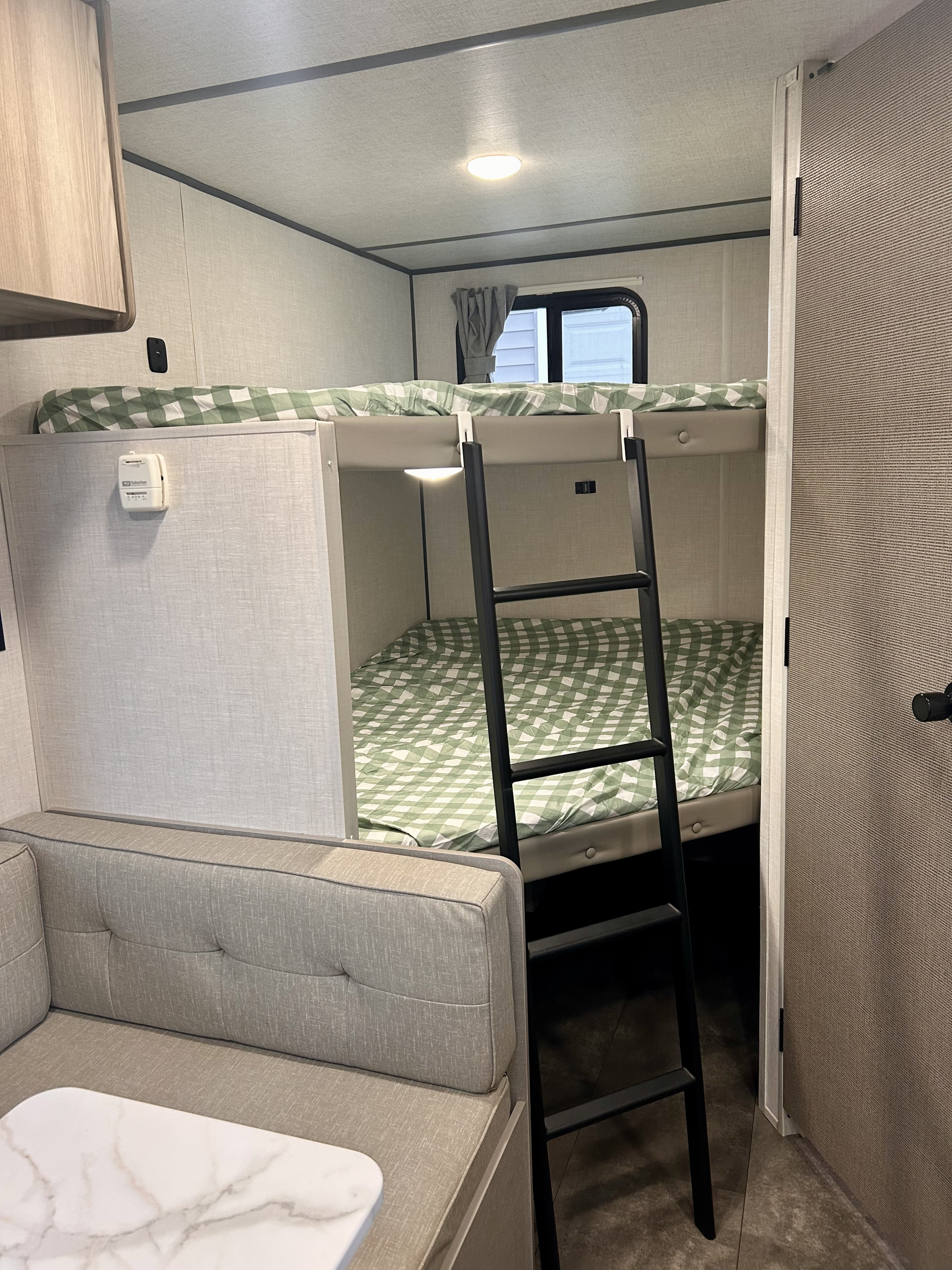 Cozy rv rental bunk beds with green checkered bedding and ladder. Features a dinette table & wall thermostat in the compact interior.. Forest River Wildwood FSX 2025
