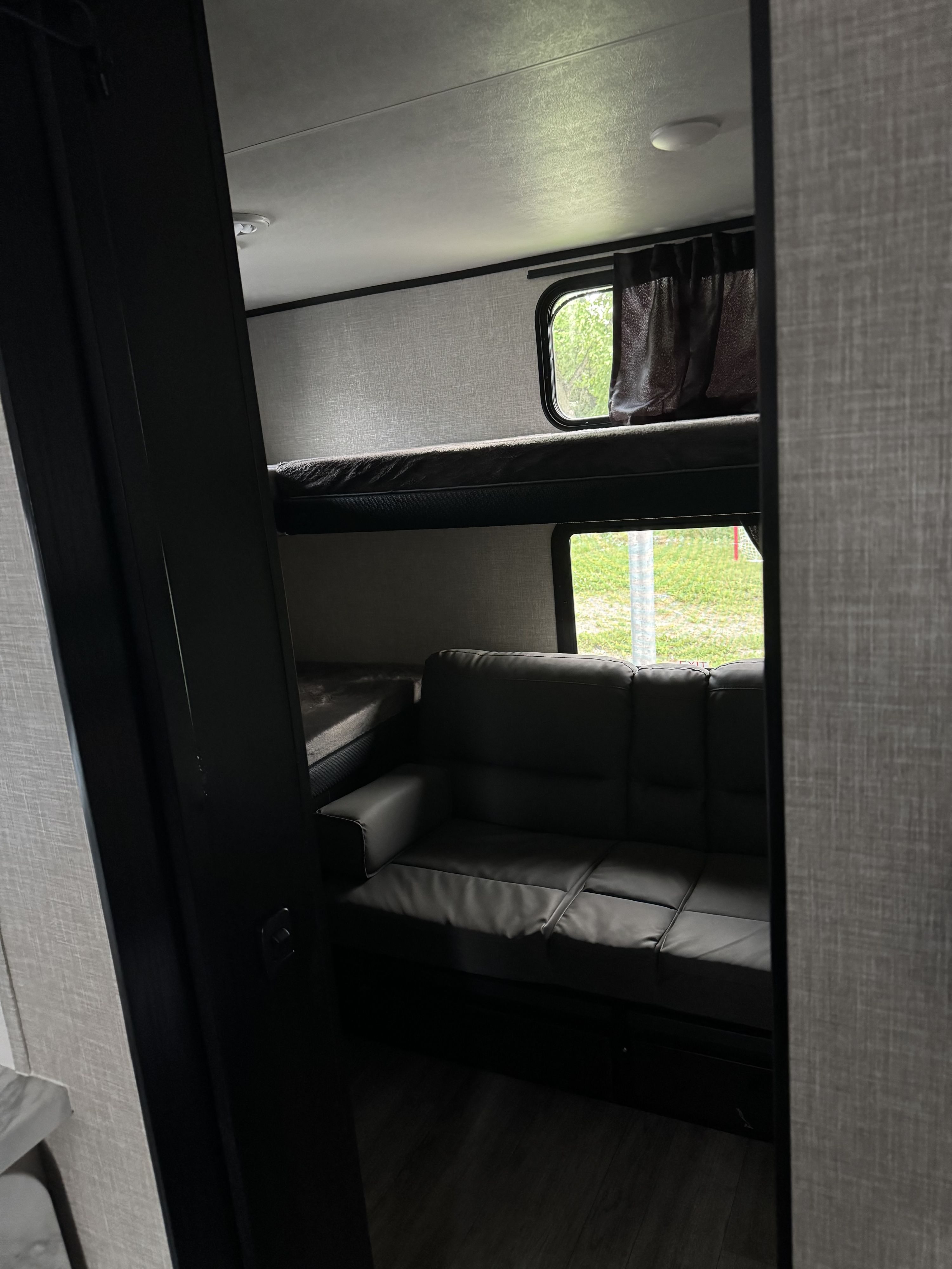 RV rental interior: bunk beds, a comfortable sofa, and bright windows with green outdoor views. Great for adventures!. Jayco 30qb 2023
