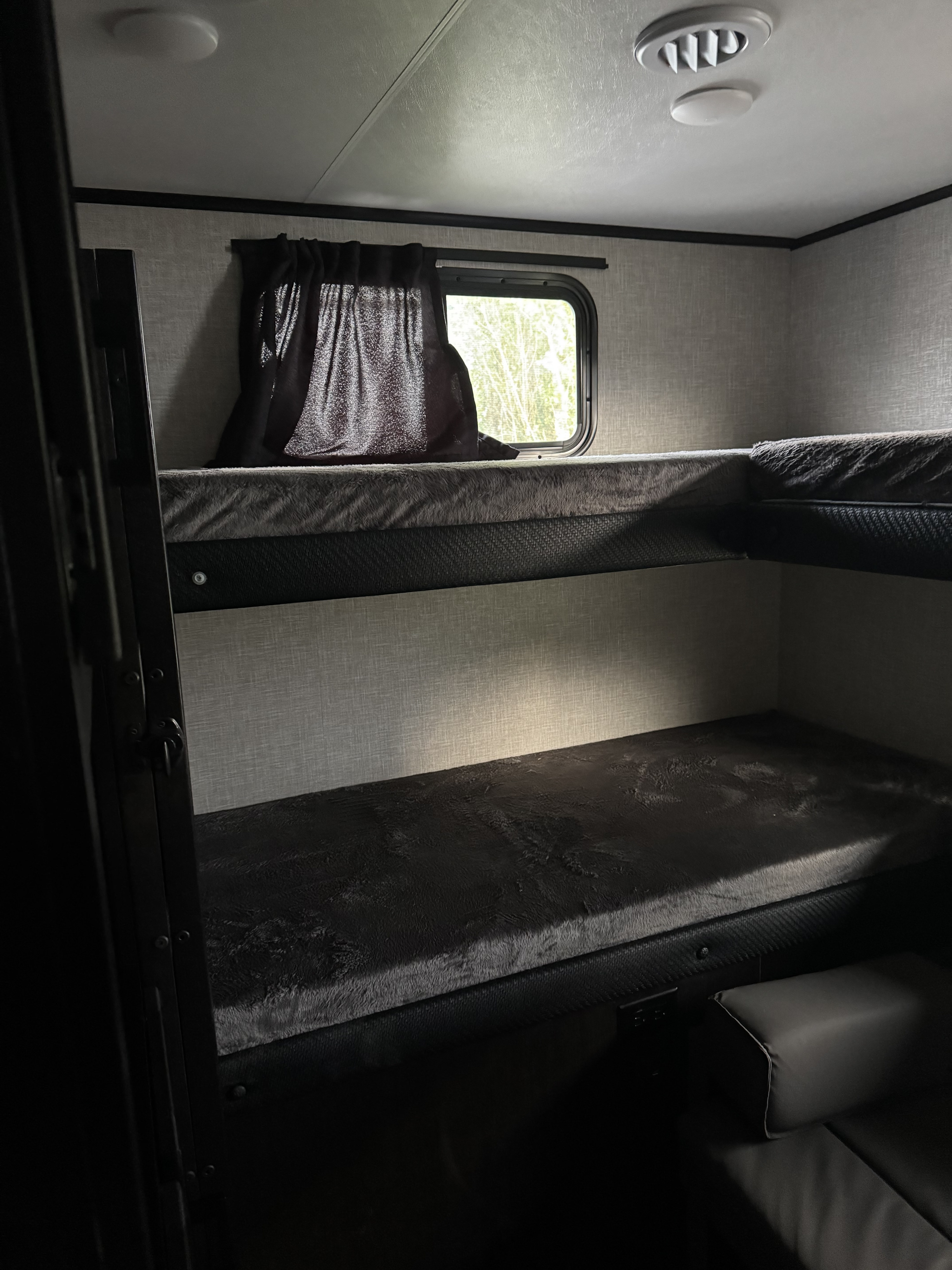RV rental interior: two-tier bunk beds with dark, plush mattresses. A window with curtains offers a bright view.. Jayco 30qb 2023